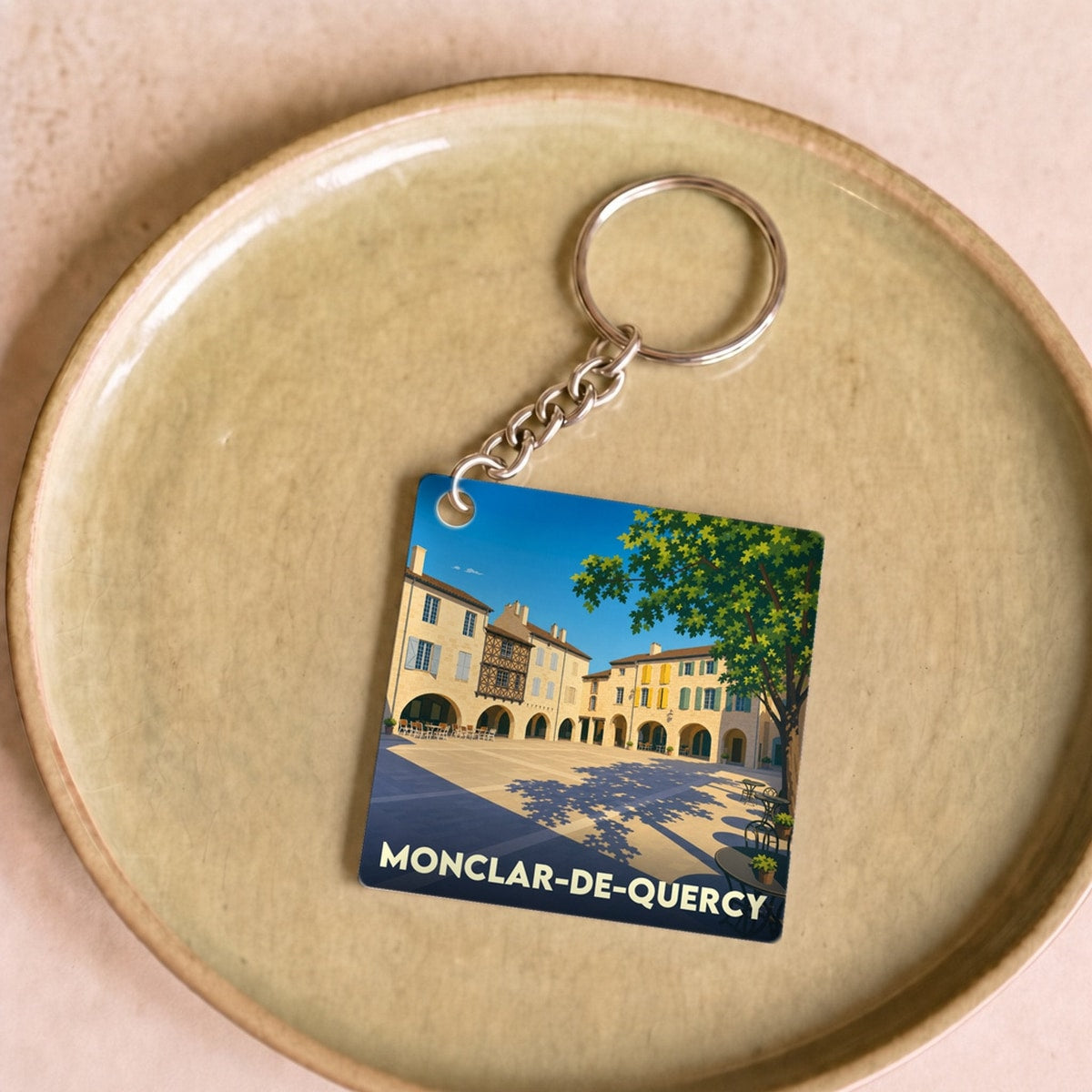 Porte-clés souvenir de la ville de Monclar-de-Quercy avec une illustration stylisée de sa place principale.