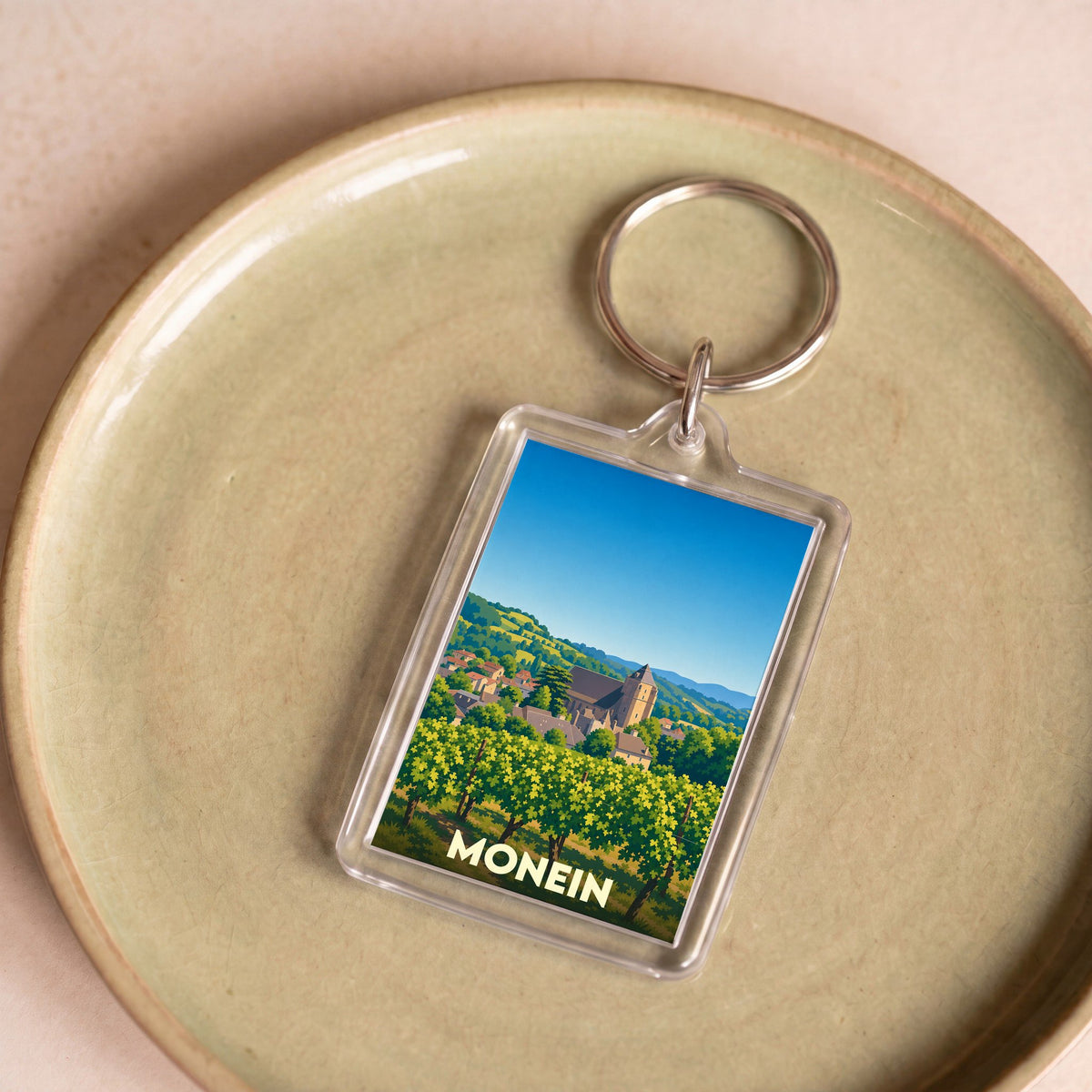 Porte-clés souvenir de la ville de Monein avec une illustration stylisée de son paysage et de son église.