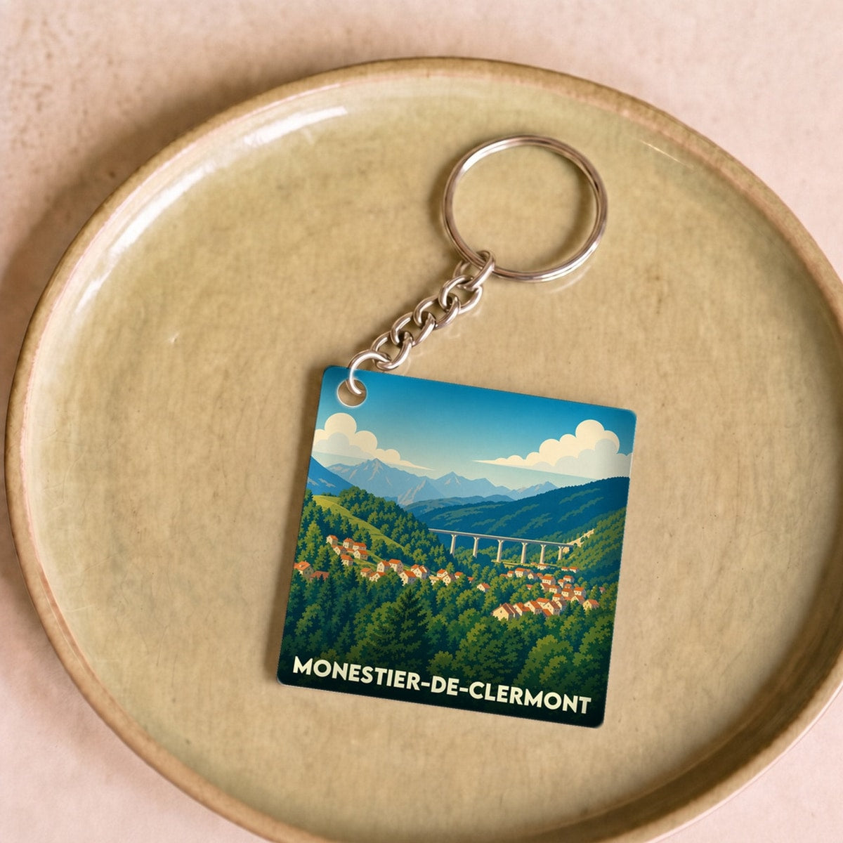 Porte-clés souvenir de la ville de Monestier-de-Clermont avec une illustration stylisée d'un paysage montagneux.