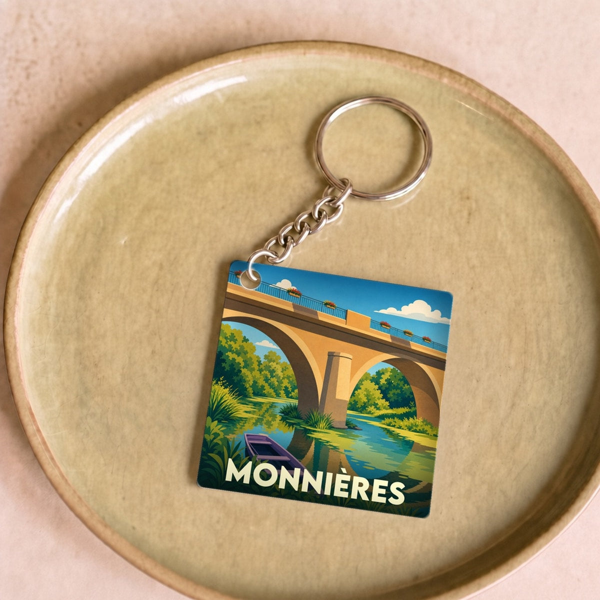 Porte-clés souvenir de la ville de Monnières avec une illustration stylisée d'un pont et d'une barque.