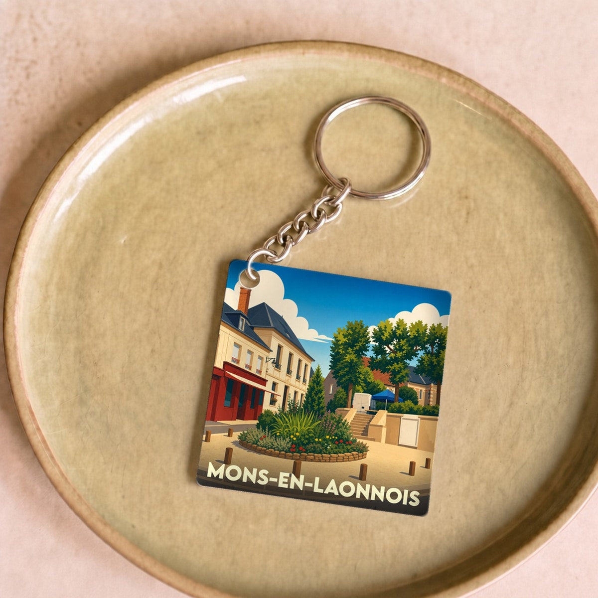 Porte-clés souvenir de la ville de Mons-en-Laonnois avec une illustration stylisée.