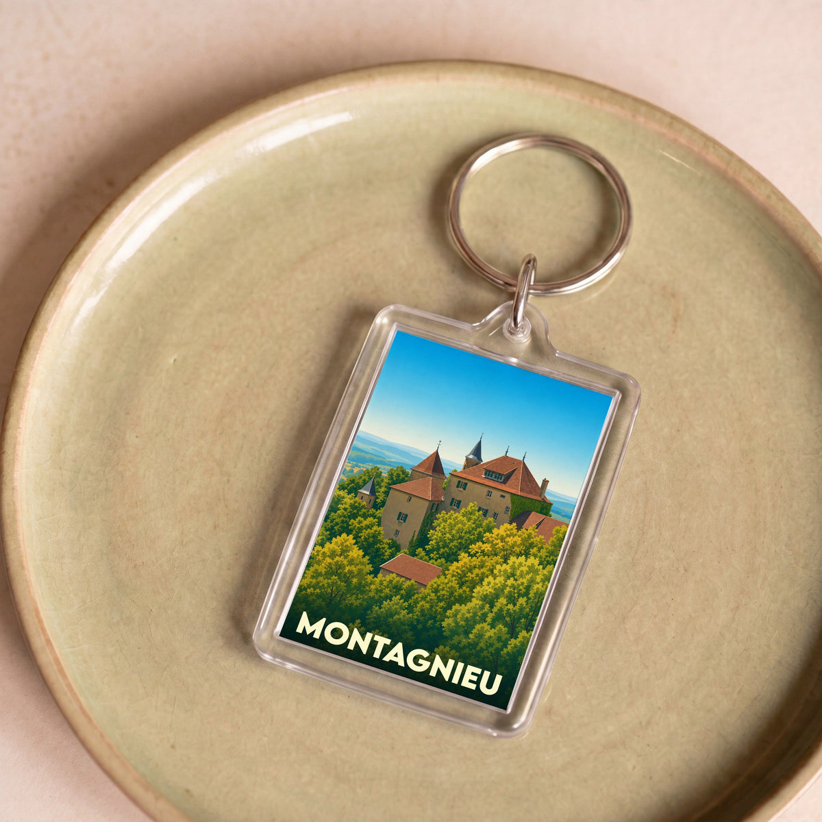 Porte-clés souvenir de la ville de Montagnieu avec une illustration stylisée d'un château entouré de verdure.