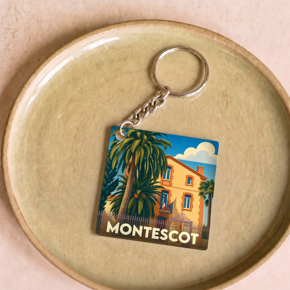 Porte-clés souvenir de la ville de Montescot avec une illustration stylisée d'une bâtisse et de palmiers.
