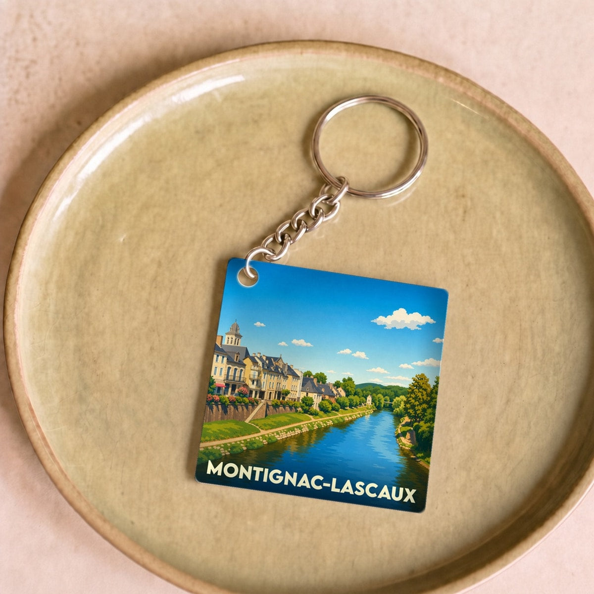 Porte-clés souvenir de Montignac-Lascaux avec une illustration stylisée de la ville et de sa rivière.