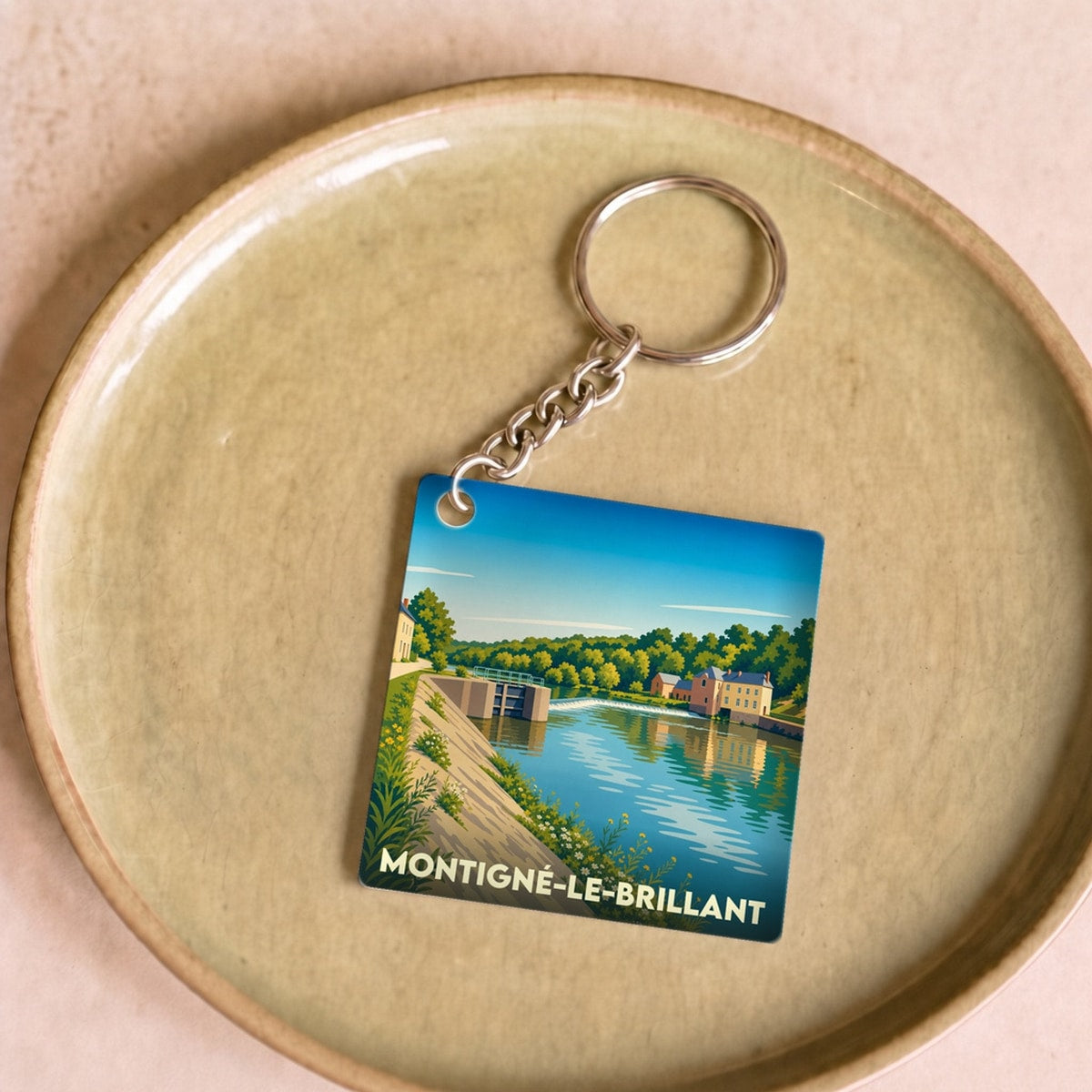 Porte-clés souvenir de la ville de Montigné-le-Brillant avec une illustration stylisée d'un paysage de rivière.