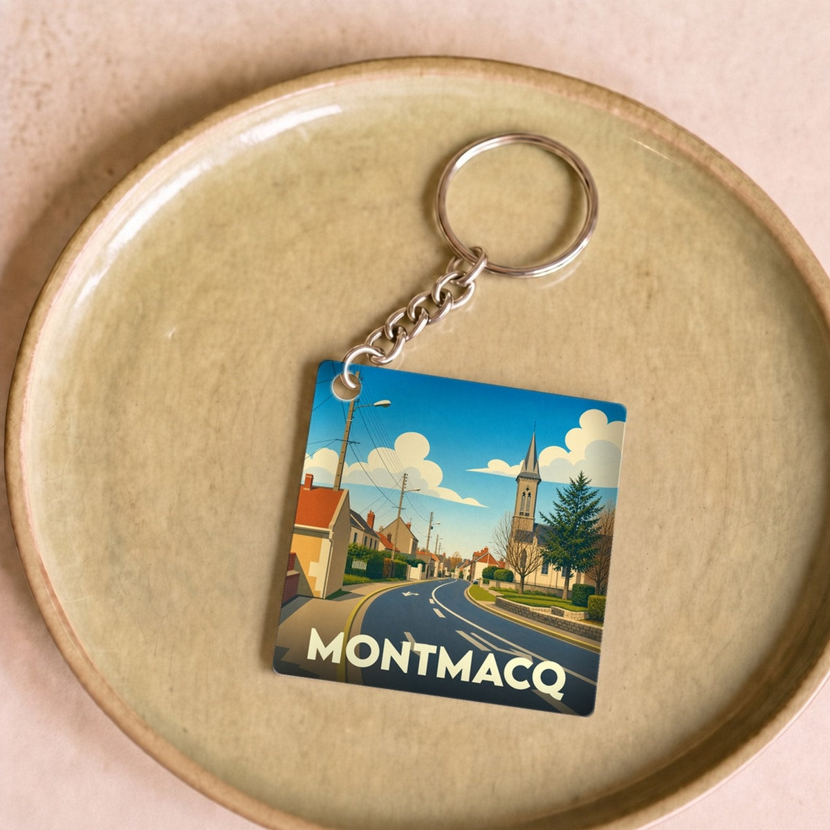 Porte-clés souvenir de la ville de Montmacq avec une illustration stylisée d'une rue du village.