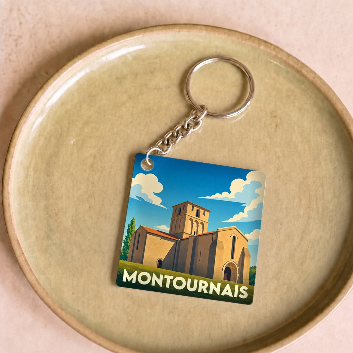 Porte-clés souvenir de la ville de Montournais avec une illustration stylisée d'un monument historique sous un ciel bleu.