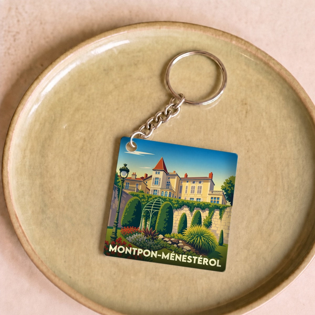 Porte-clés souvenir de la ville de Montpon-Ménestérol avec une illustration stylisée d'un domaine fleuri.