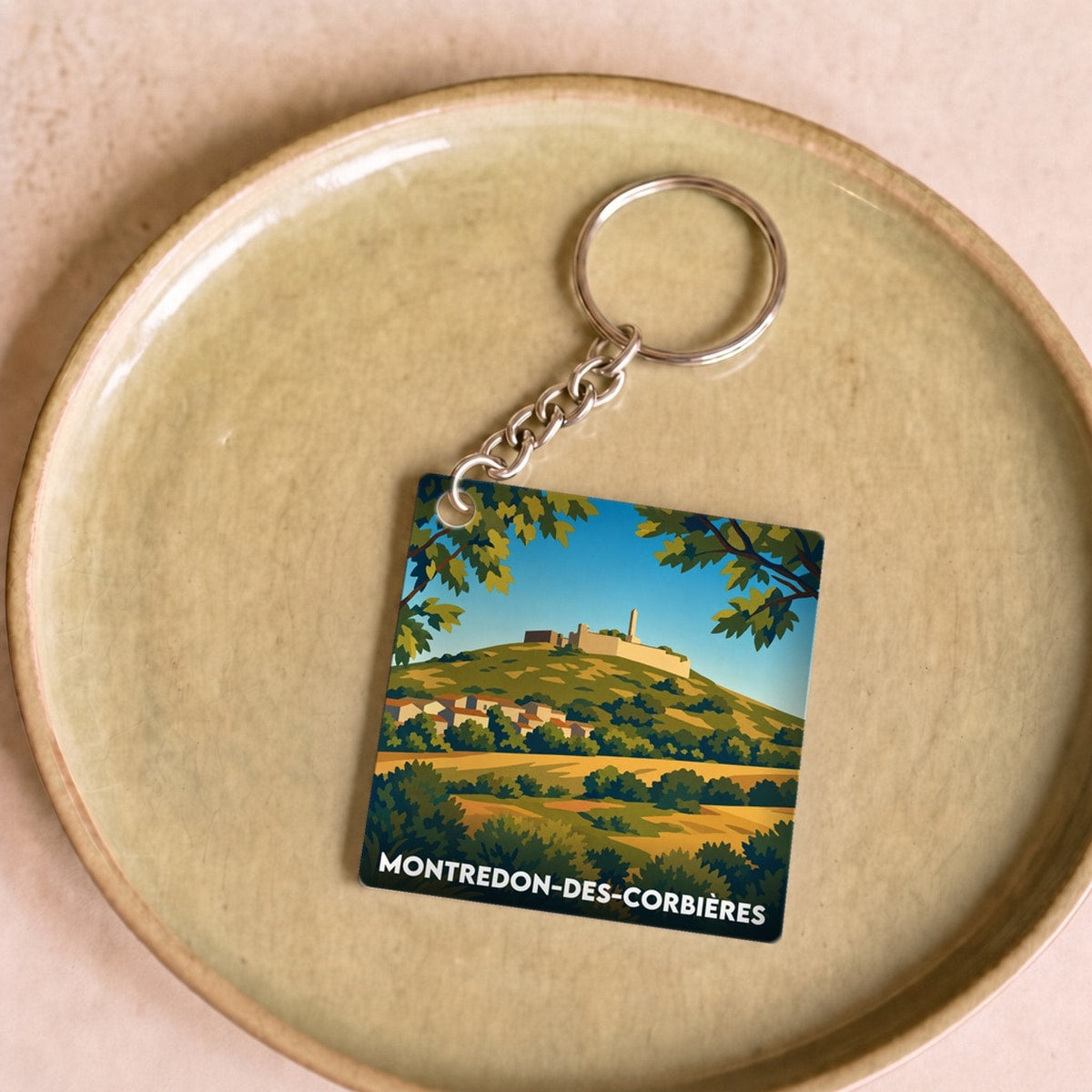 Porte-clés souvenir de la ville de Montredon-des-Corbières avec une illustration de paysage stylisée.