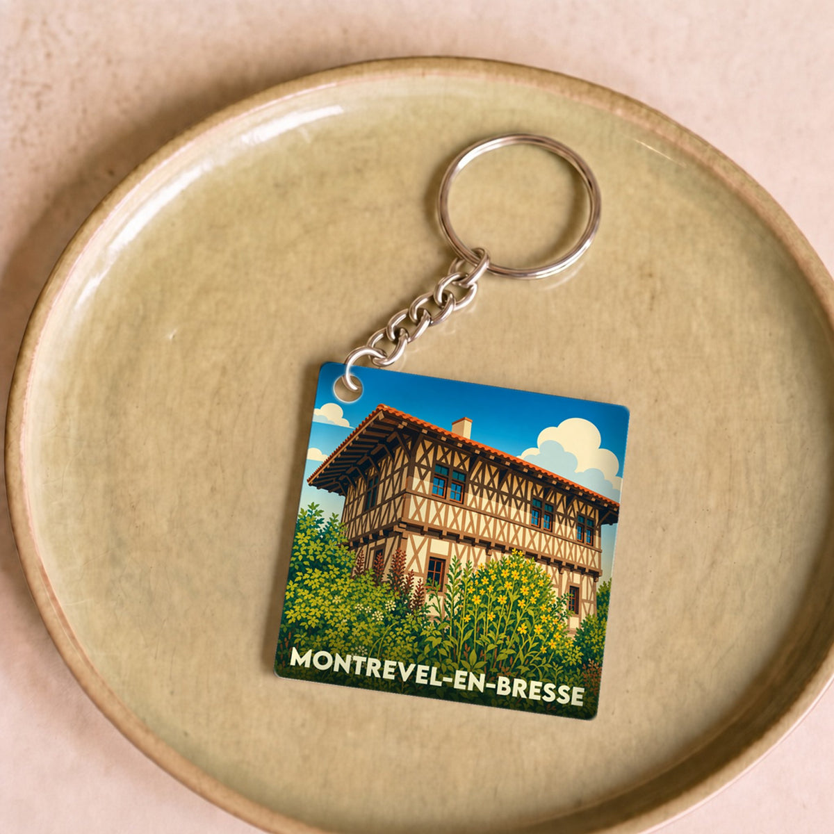 Porte-clés souvenir de la ville de Montrevel-en-Bresse avec une illustration stylisée d'une maison à colombages.
