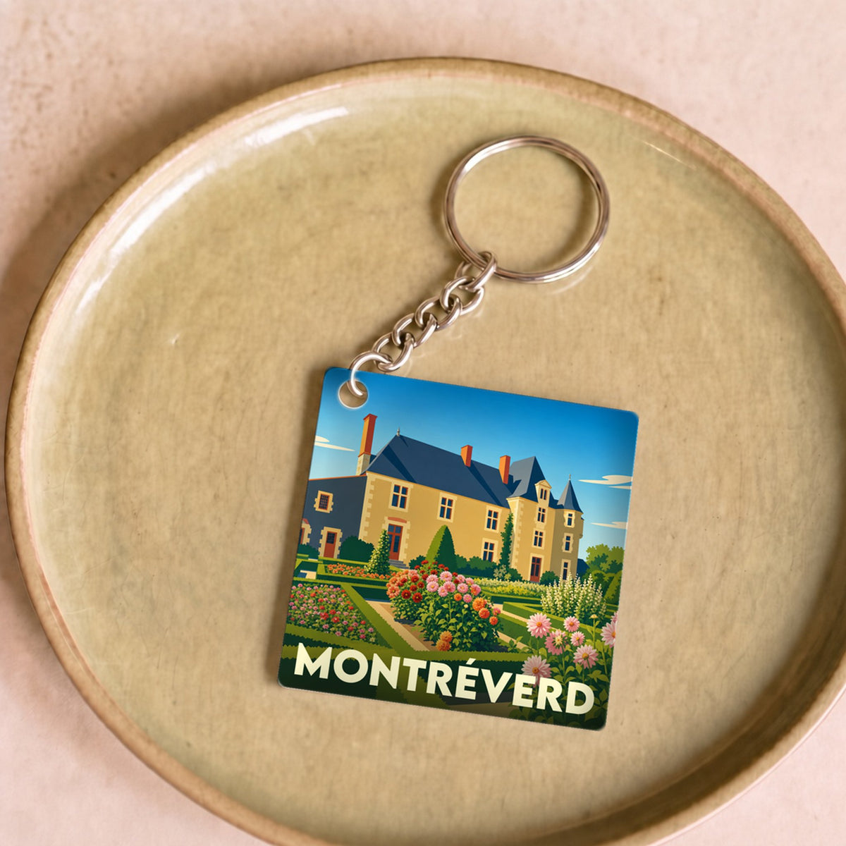 Porte-clés souvenir de la ville de Montréverd avec une illustration stylisée d'un château et de ses jardins fleuris.