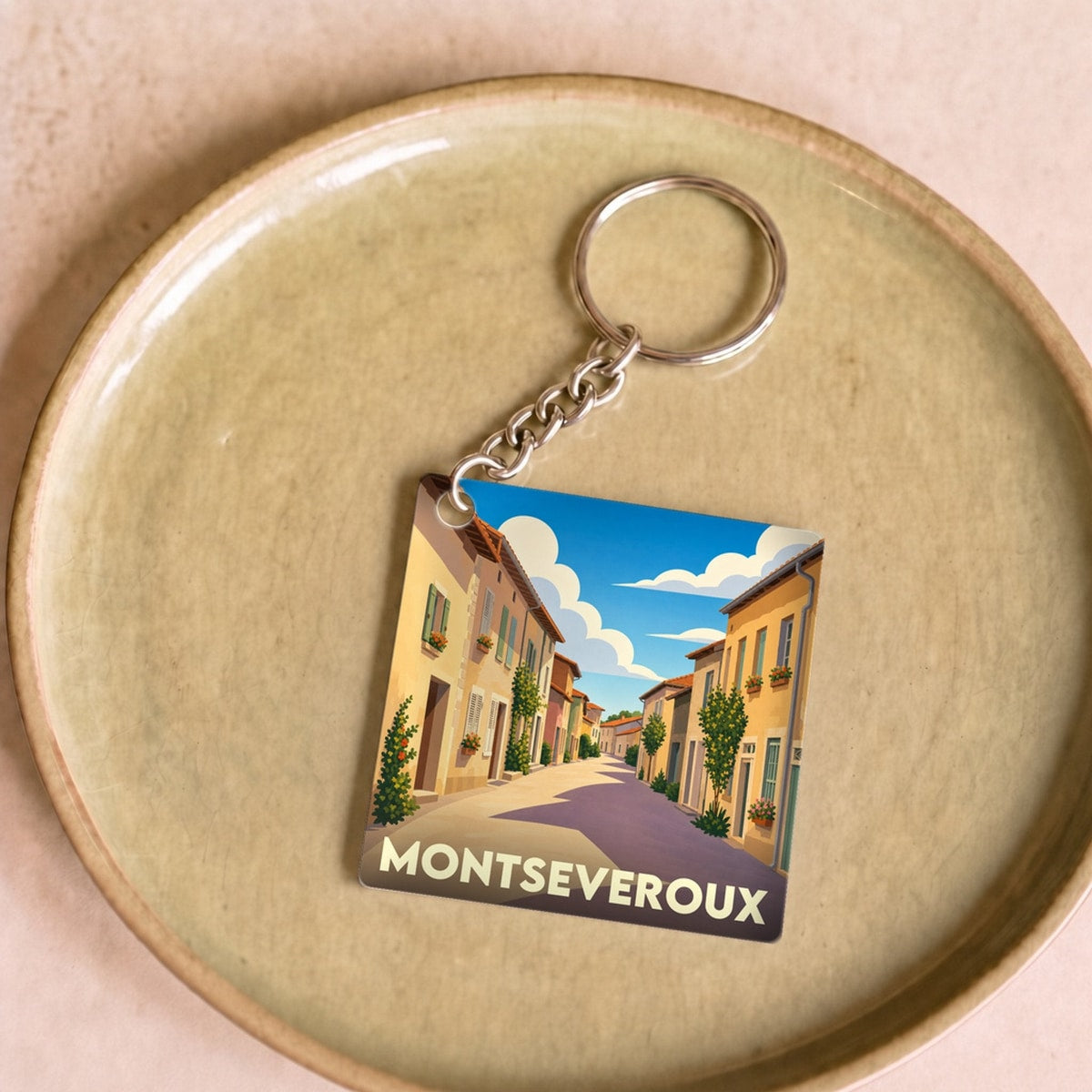 Porte-clés souvenir de la ville de Montseveroux avec une illustration stylisée d'une rue ensoleillée.