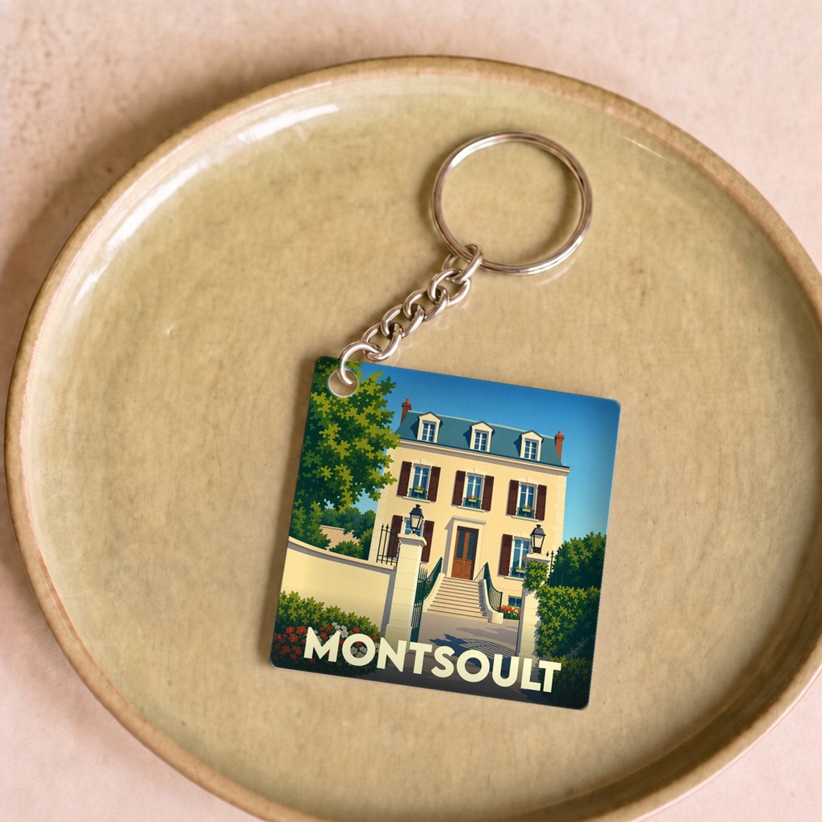 Porte-clés souvenir de la ville de Montsoult avec une illustration stylisée d'une demeure bourgeoise.