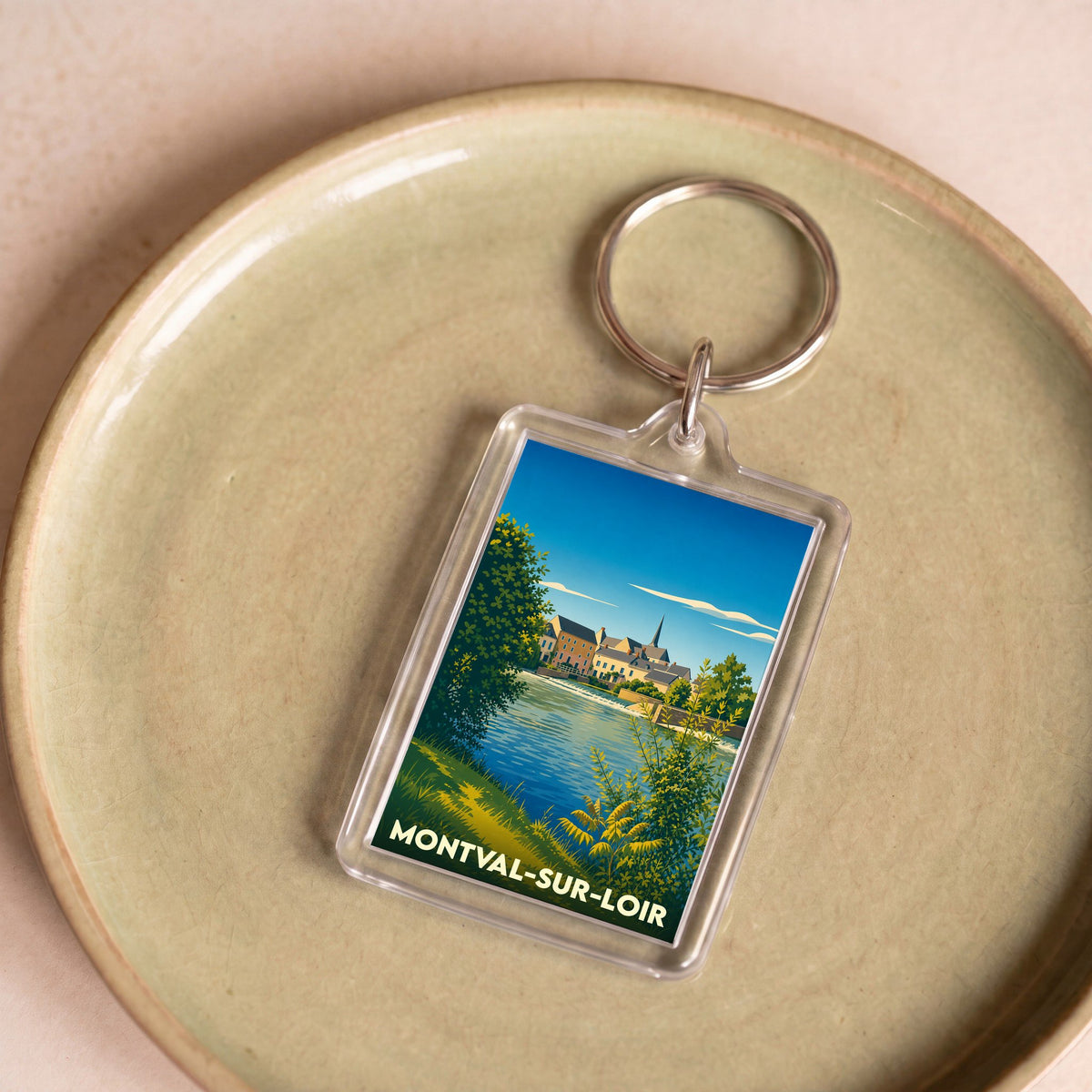 Porte-clés souvenir de la ville de Montval-sur-Loir avec une illustration stylisée d'un paysage de bord de rivière.