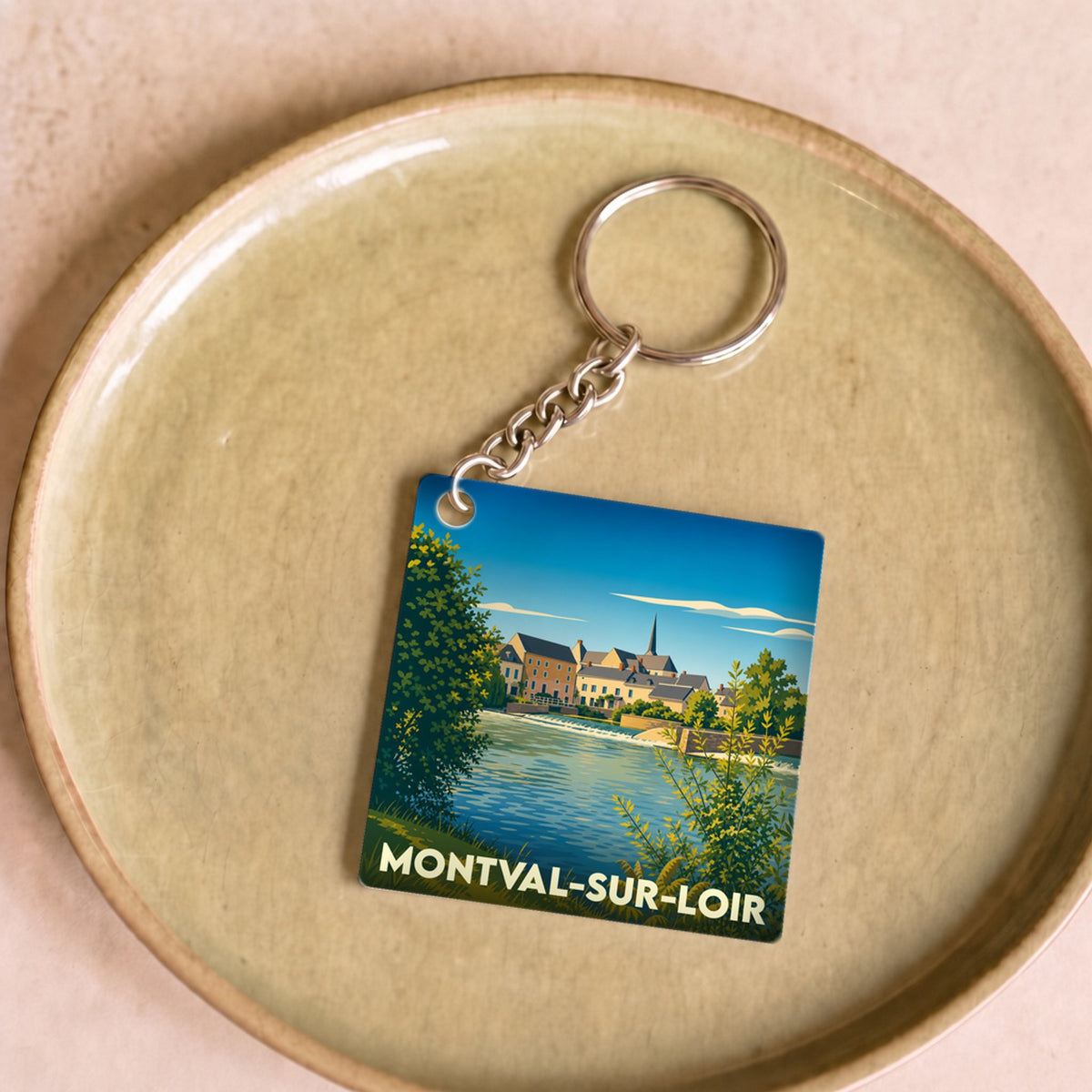 Porte-clés souvenir de la ville de Montval-sur-Loir avec une illustration stylisée d'un paysage de bord de rivière.