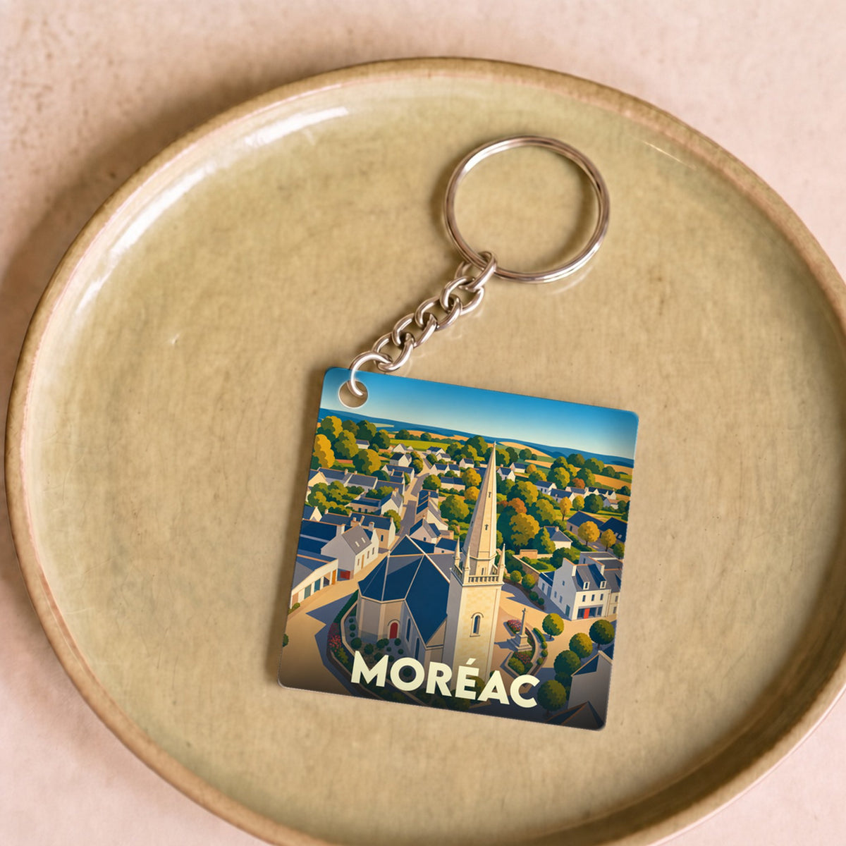 Porte-clés souvenir de la ville de Moréac avec une illustration stylisée montrant l'église et les maisons.