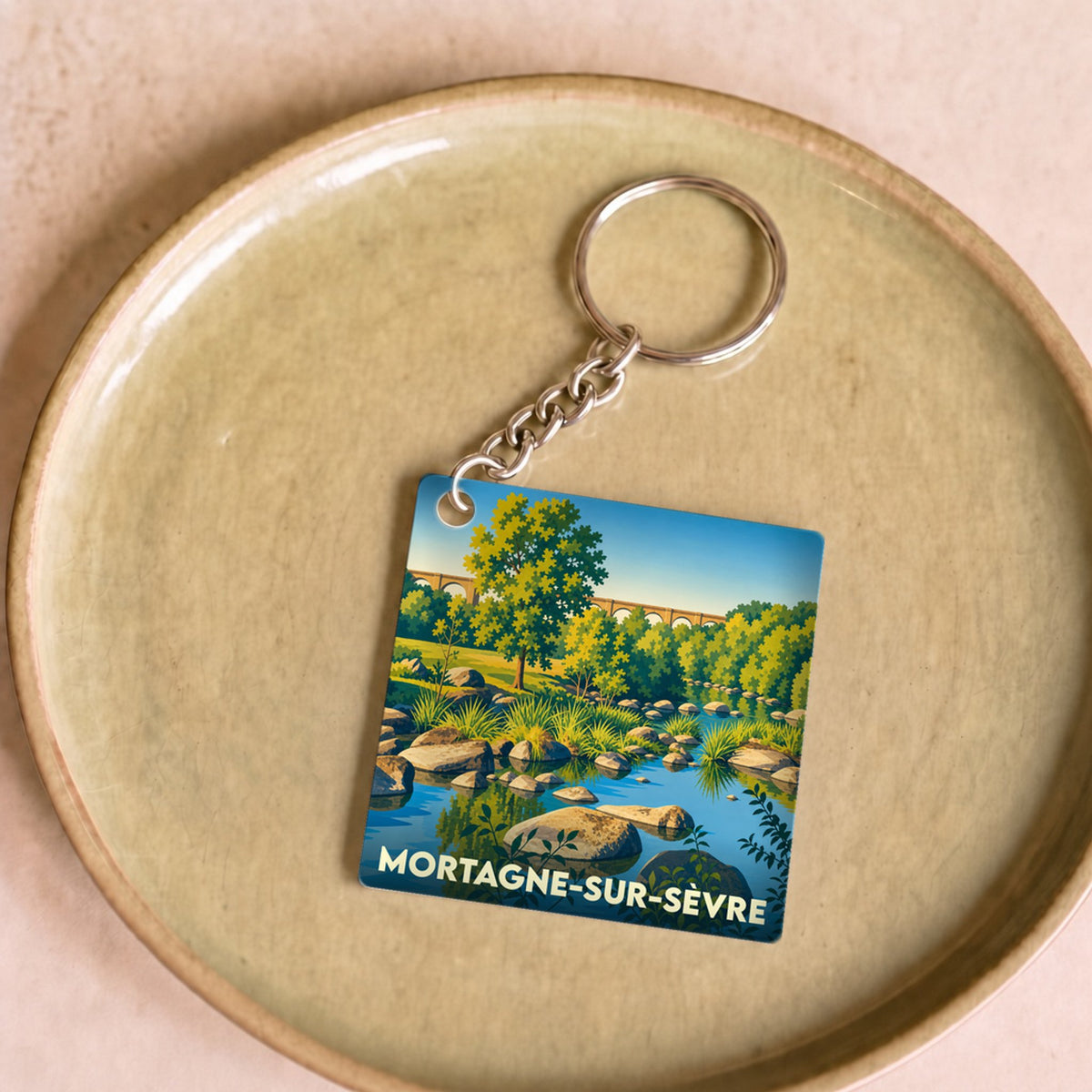 Porte-clés souvenir de la ville de Mortagne-sur-Sèvre avec une illustration stylisée d'un paysage de rivière.