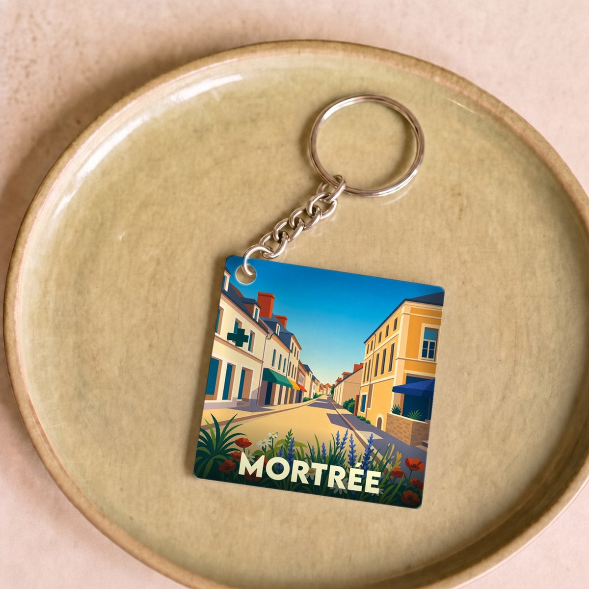 Porte-clés souvenir de la ville de Mortrée avec une illustration stylisée d'une rue ensoleillée.
