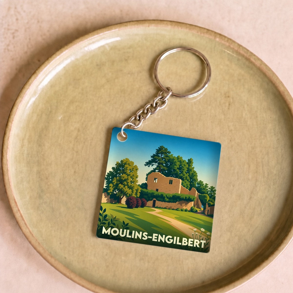 Porte-clés souvenir de la ville de Moulins-Engilbert avec une illustration stylisée d'un paysage historique.
