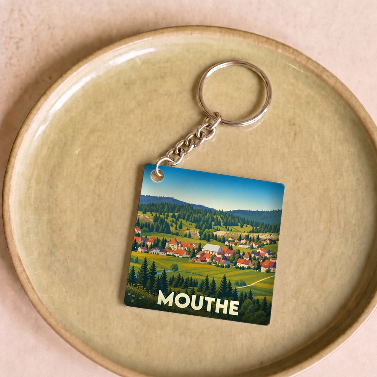 Porte-clés souvenir de la ville de Mouthe avec une illustration stylisée de son paysage montagnard.