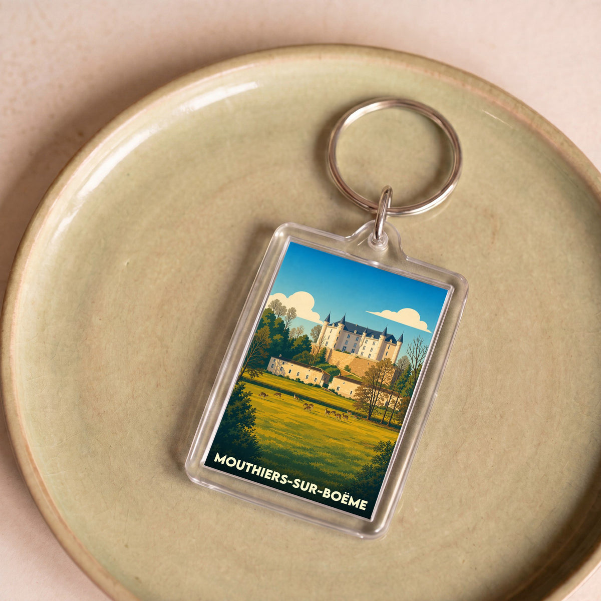 Porte-clés souvenir de Mouthiers-sur-Boëme avec une illustration stylisée de son château et de sa campagne.
