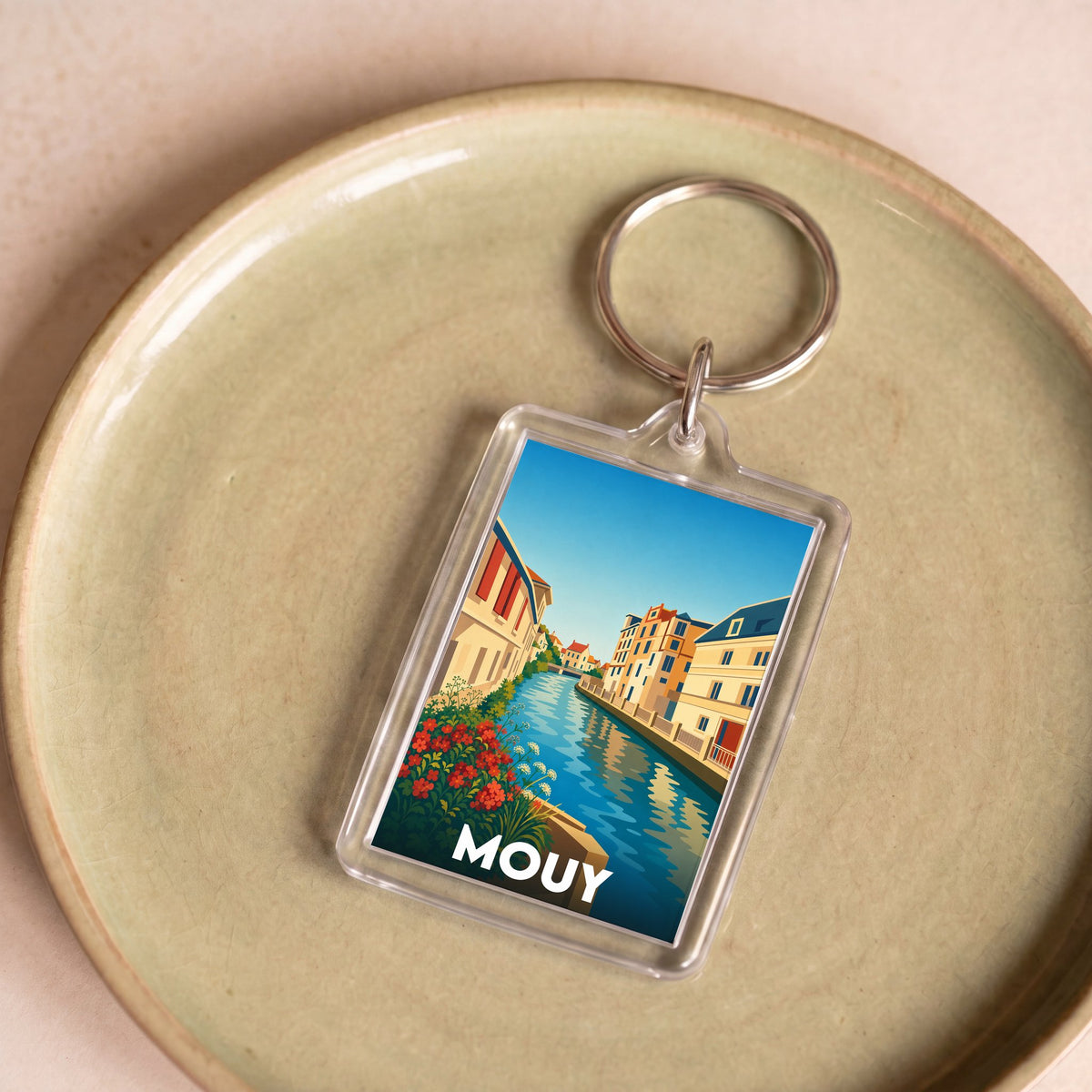 Porte-clés souvenir de la ville de Mouy avec une illustration stylisée d'un canal et de bâtiments colorés.