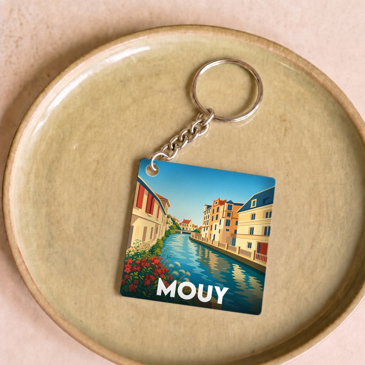Porte-clés souvenir de la ville de Mouy avec une illustration stylisée d'un canal et de bâtiments colorés.