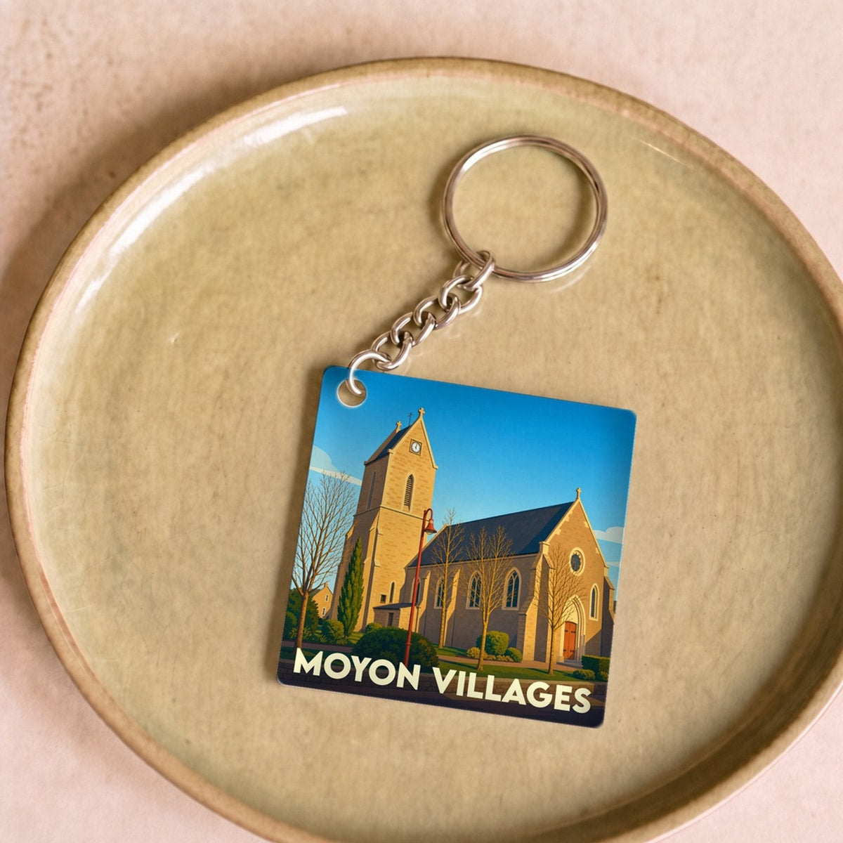 Porte-clés souvenir de la commune de Moyon Villages avec une illustration stylisée de son église.