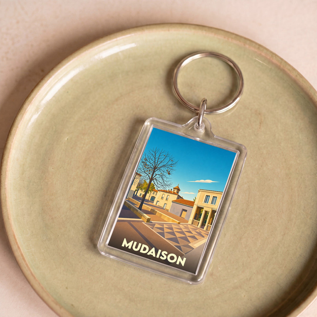 Porte-clés souvenir de la ville de Mudaison avec une illustration stylisée.