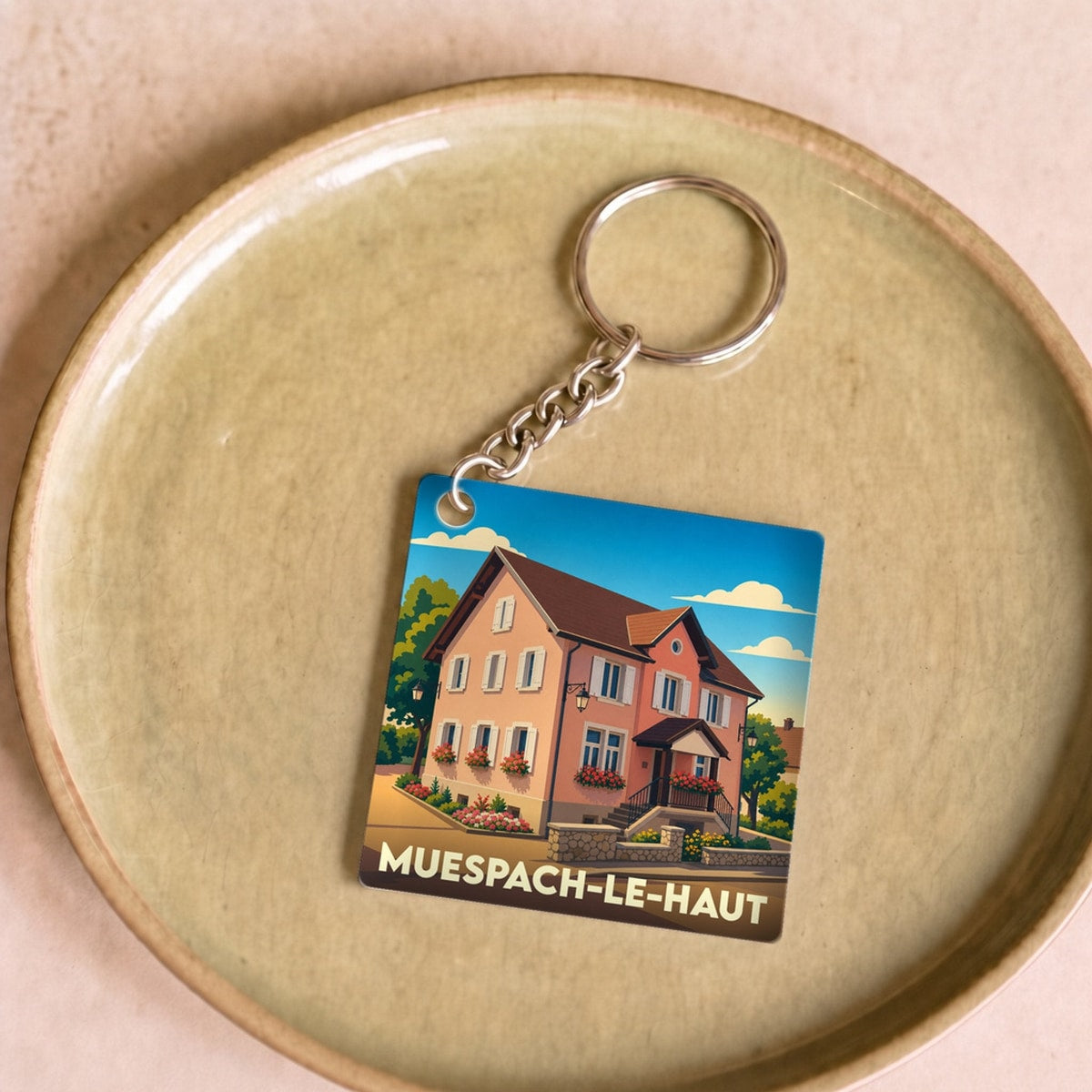 Porte-clés souvenir de la ville de Muespach-le-Haut avec une illustration stylisée d'une maison alsacienne.