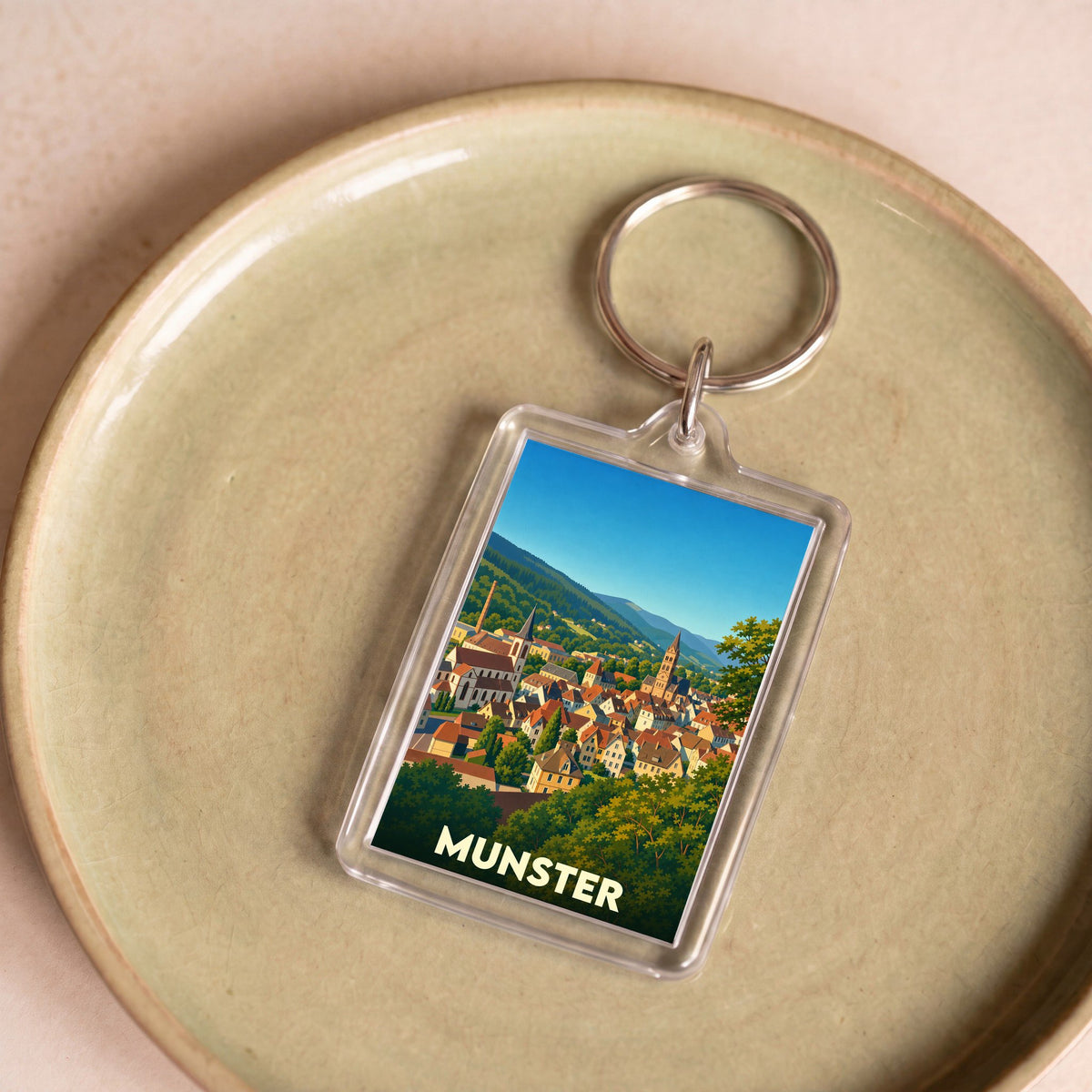 Porte-clés souvenir de la ville de Munster illustrant un panorama coloré et boisé de la cité.