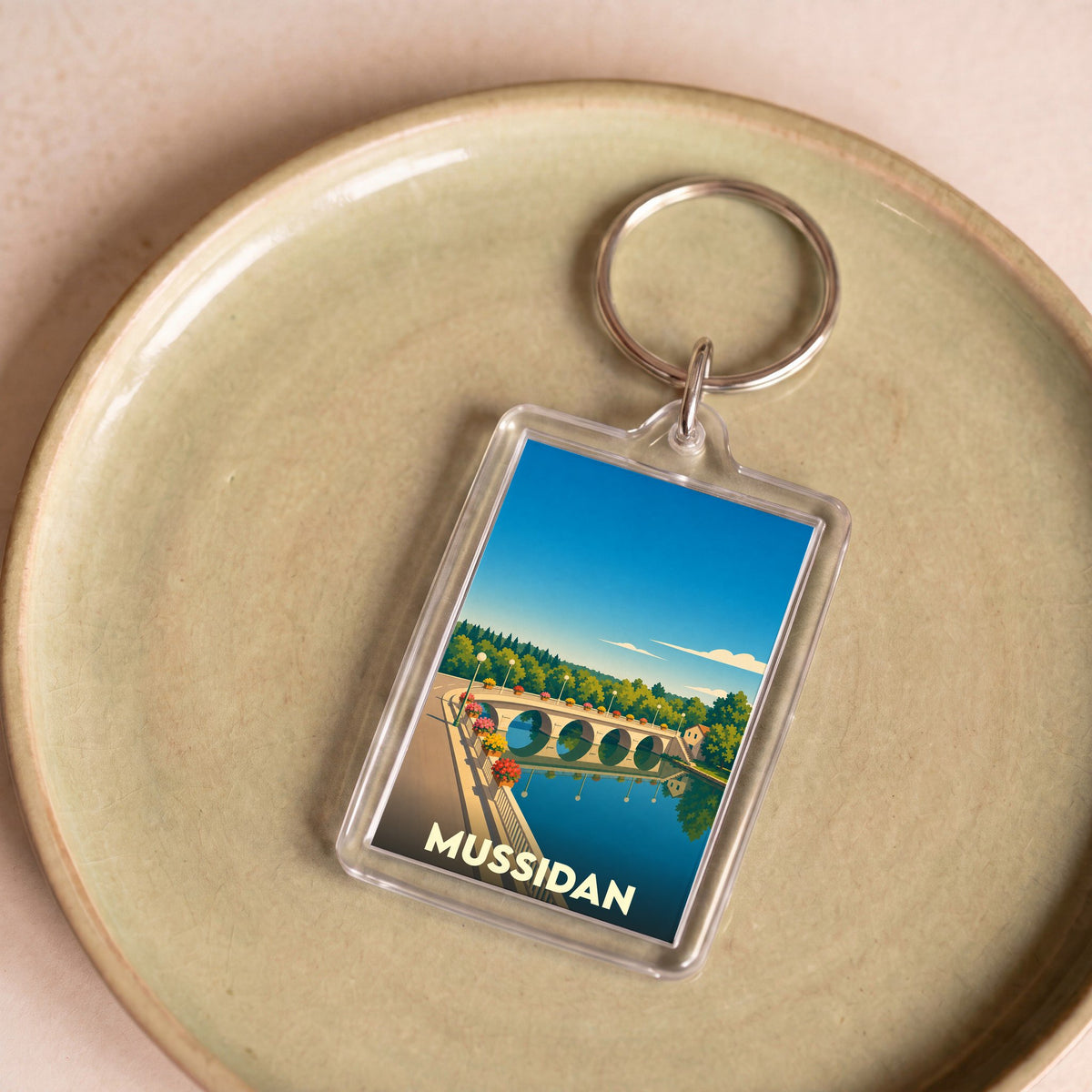 Porte-clés souvenir de la ville de Mussidan avec une illustration stylisée d'un pont sur une rivière.