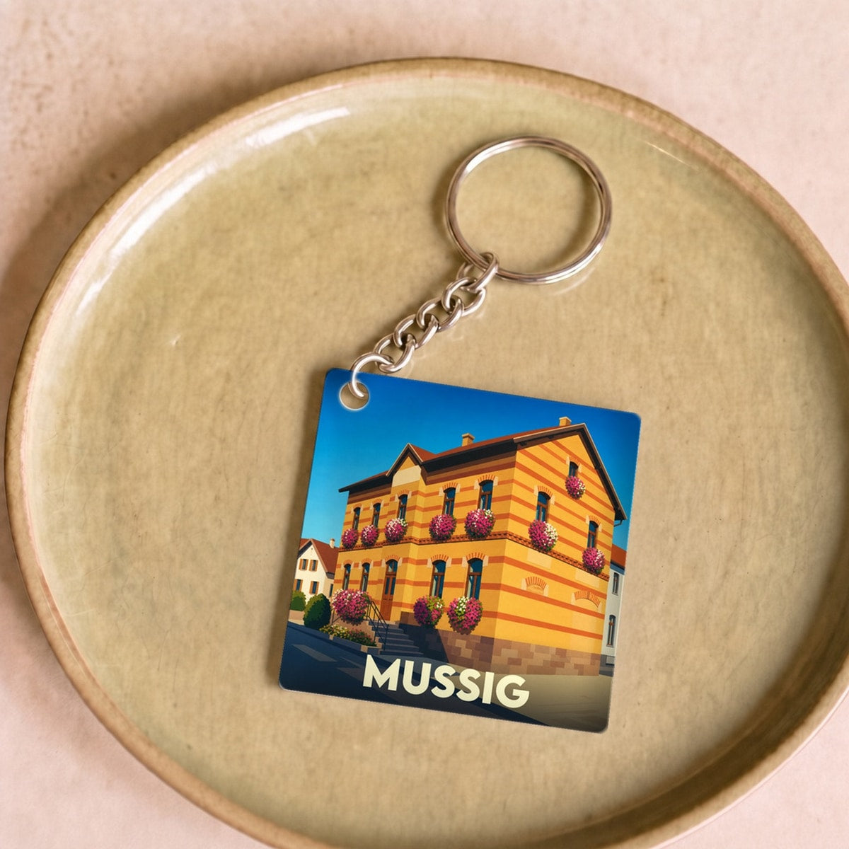 Porte-clés souvenir de la ville de Mussig avec une illustration stylisée de sa mairie fleurie.