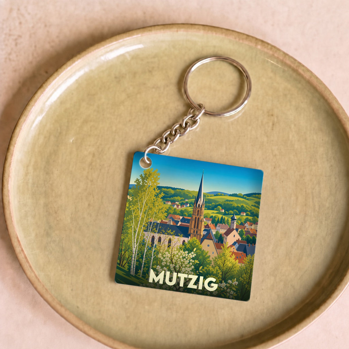 Porte-clés souvenir de la ville de Mutzig avec une illustration stylisée d'un paysage urbain alsacien.