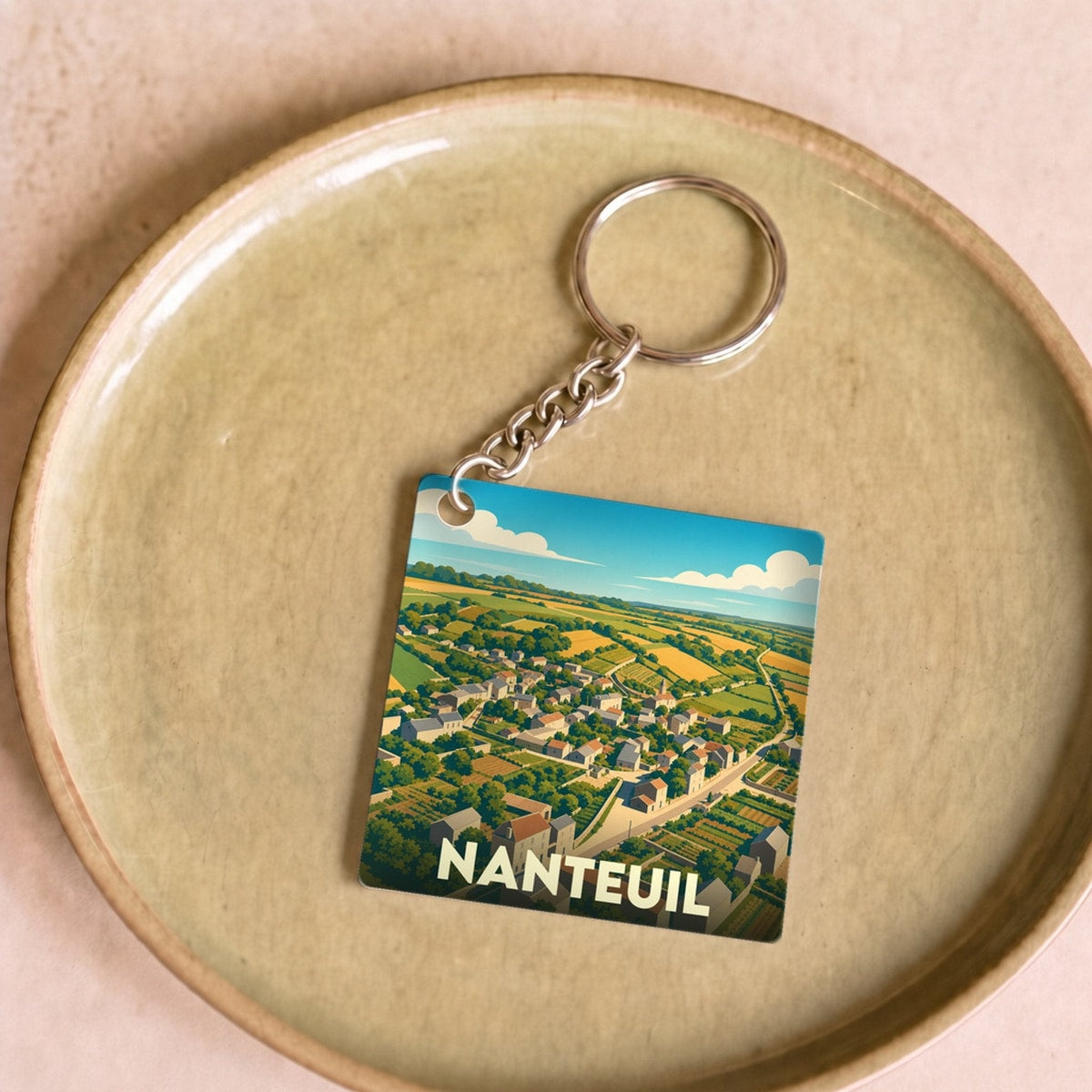 Porte-clés souvenir de la ville de Nanteuil avec une illustration stylisée d'un paysage rural.