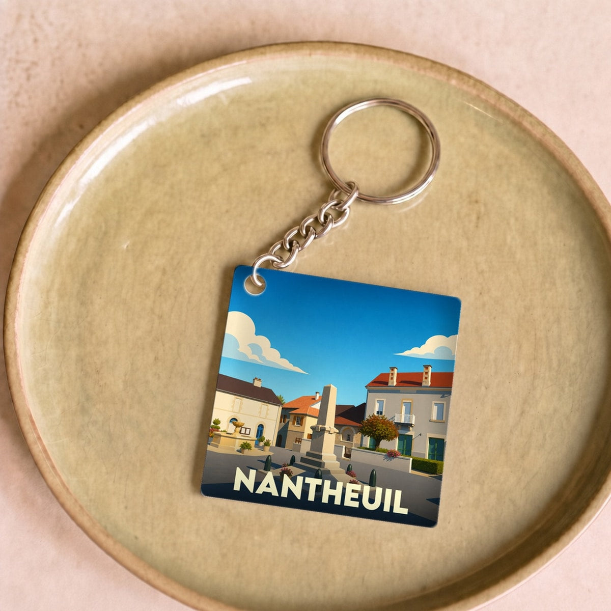 Porte-clés souvenir de la ville de Nantheuil avec une illustration stylisée d'une place ensoleillée.