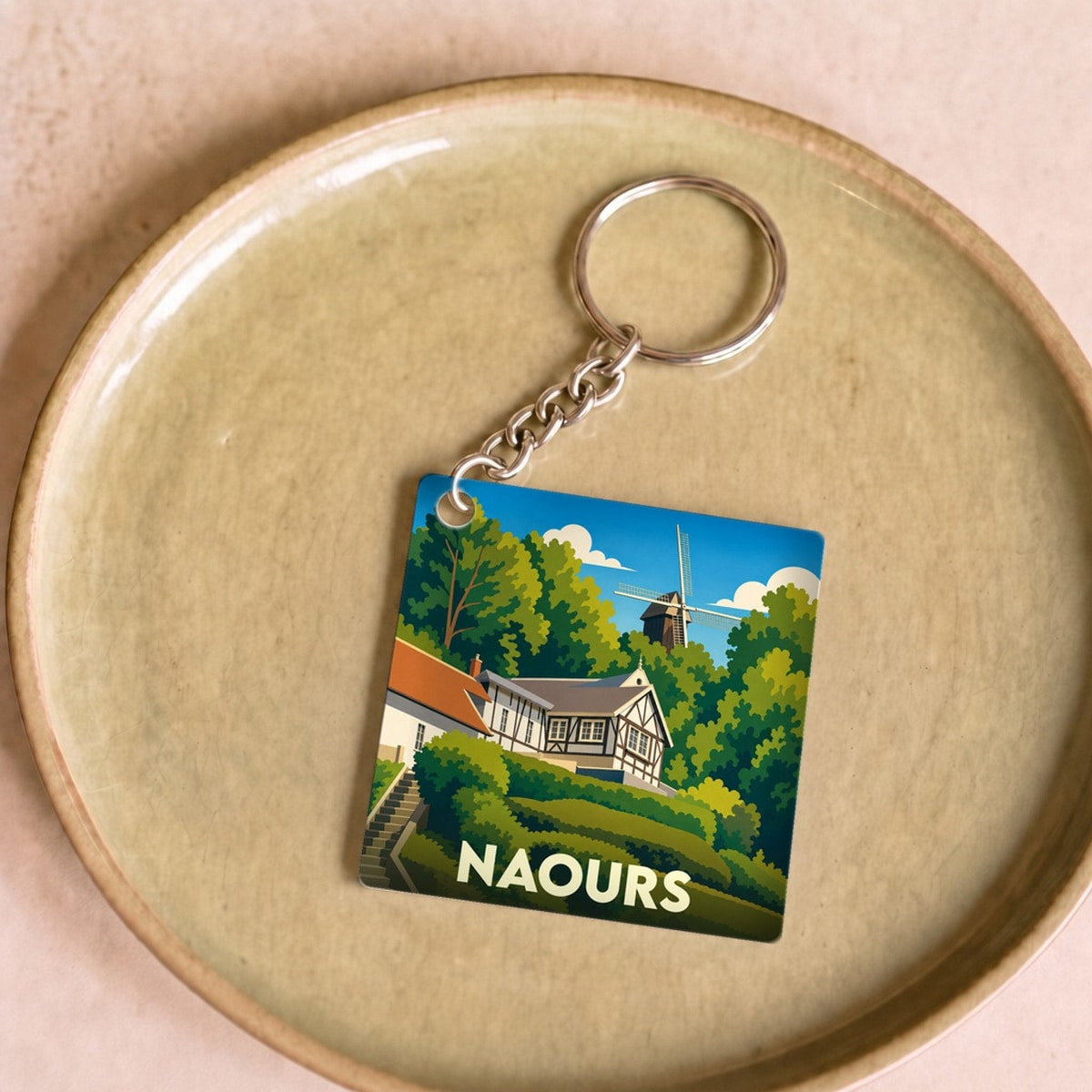 Porte-clés souvenir de la ville de Naours avec une illustration stylisée d'un paysage verdoyant et d'un moulin.