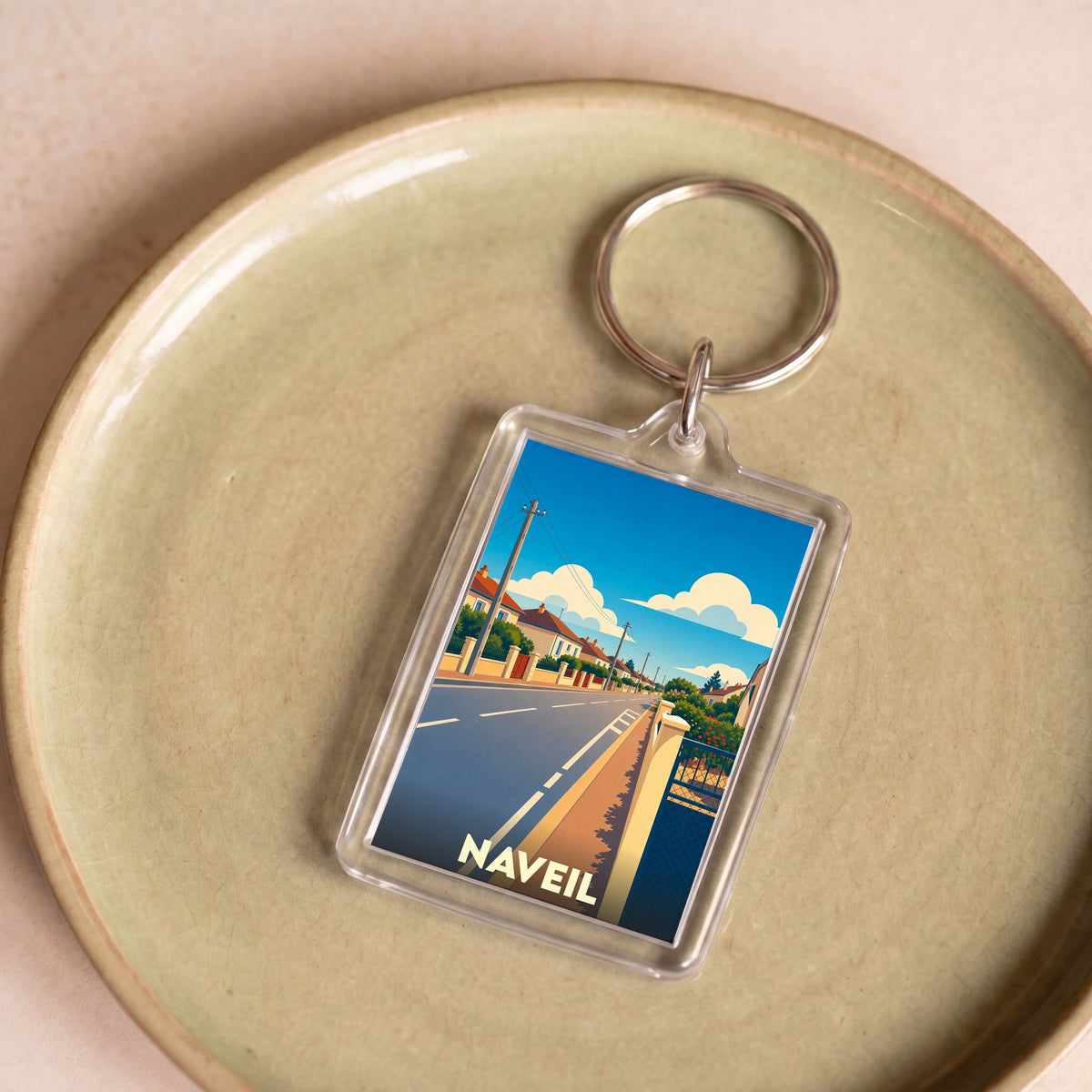 Porte-clés souvenir de la ville de Naveil avec une illustration stylisée d'une rue ensoleillée.