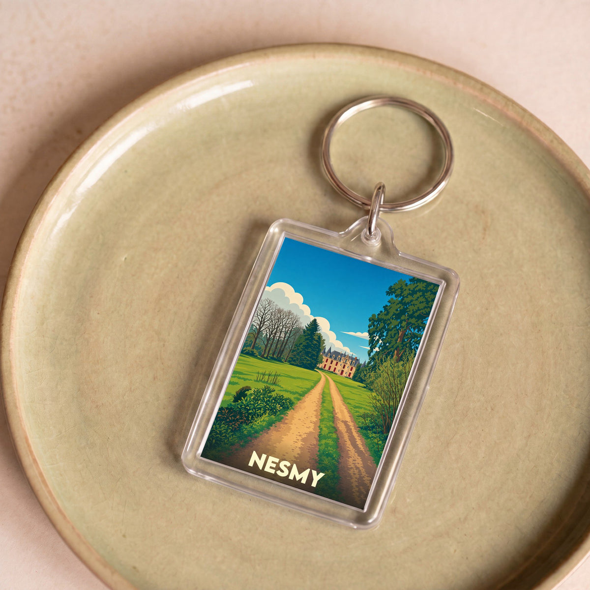 Porte-clés souvenir de la ville de Nesmy avec une illustration stylisée d'un château au bout d'un chemin.