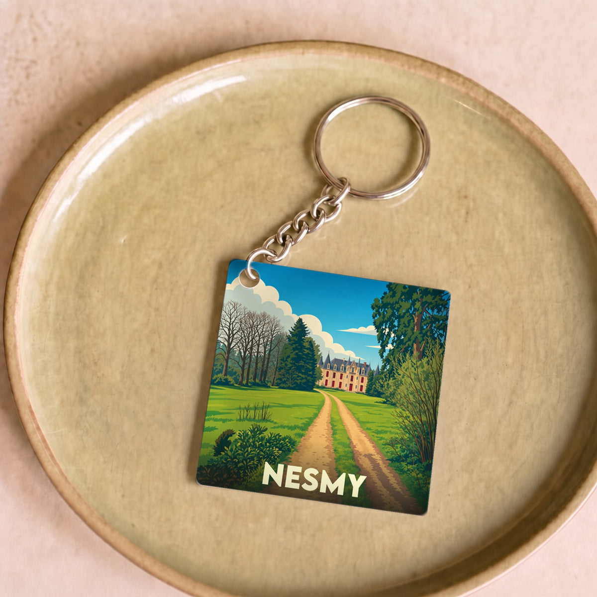 Porte-clés souvenir de la ville de Nesmy avec une illustration stylisée d'un château au bout d'un chemin.