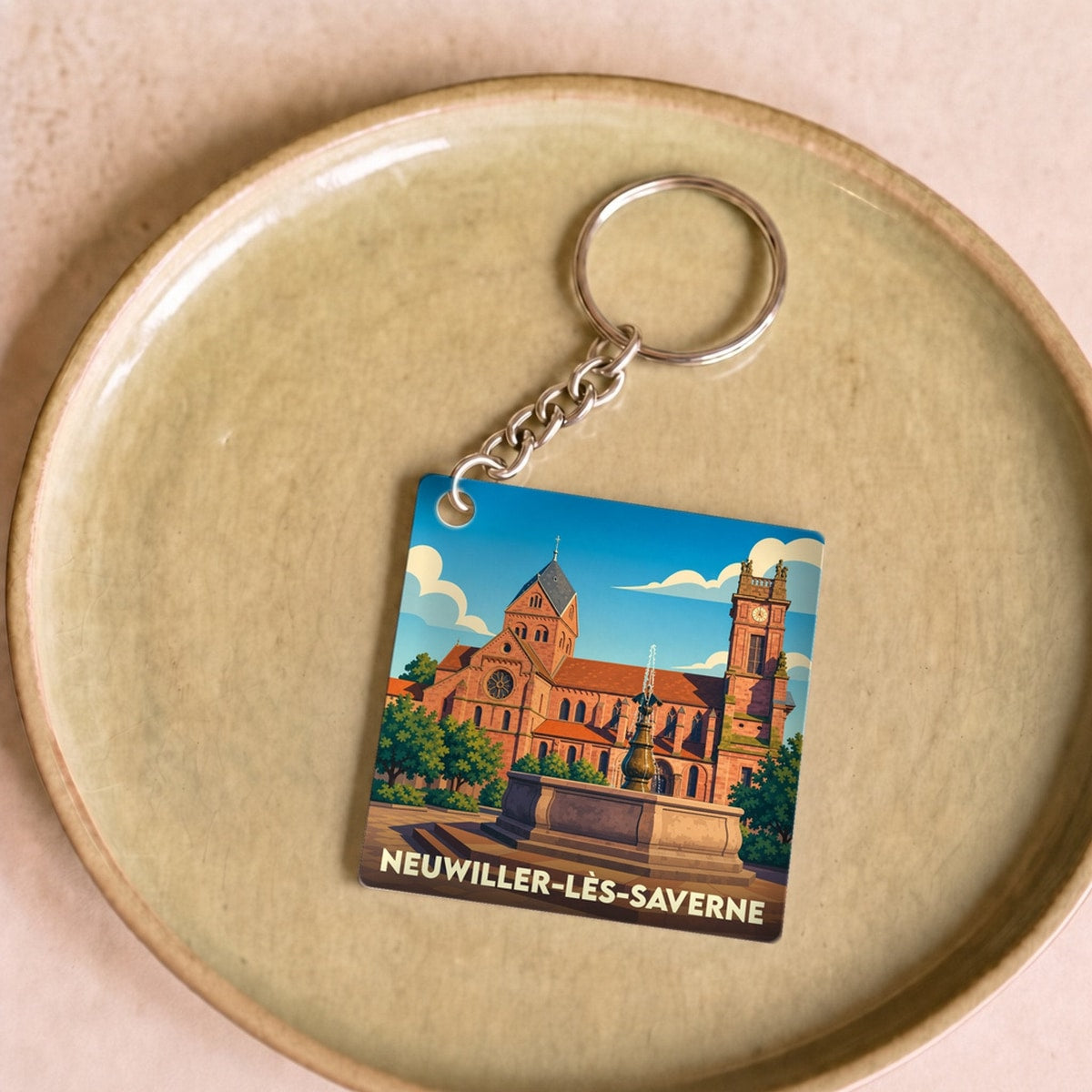 Porte-clés souvenir de la ville de Neuwiller-lès-Saverne avec une illustration stylisée de son église et d'une fontaine.