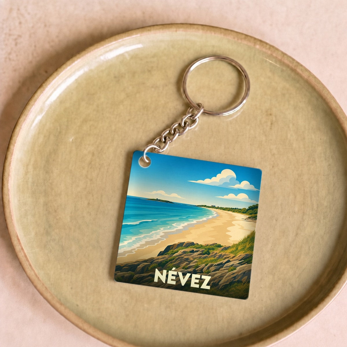 Porte-clés souvenir de la ville de Névez avec une illustration stylisée de sa plage et de sa côte rocheuse.