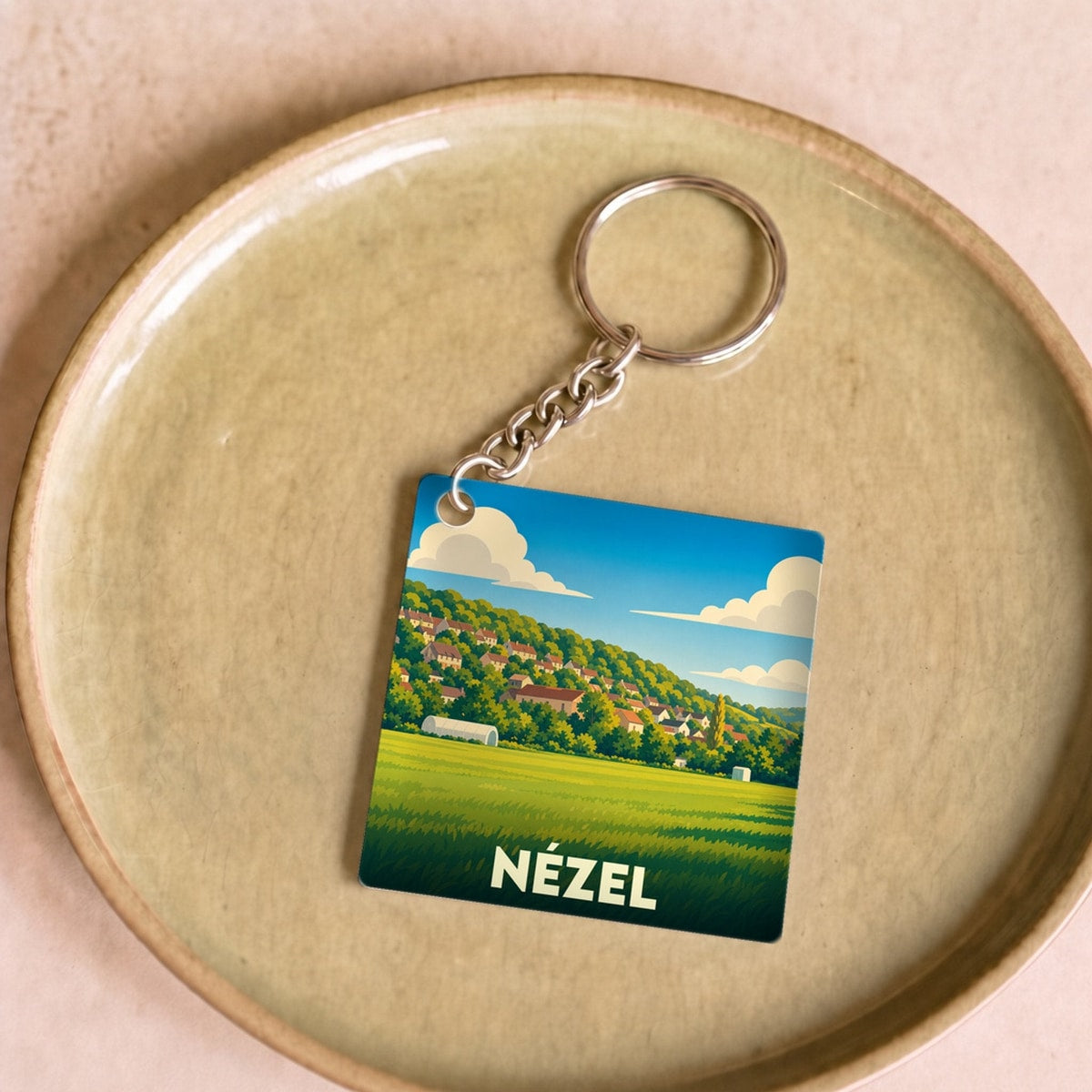 Porte-clés souvenir de la ville de Nézel avec une illustration stylisée de son paysage vallonné.