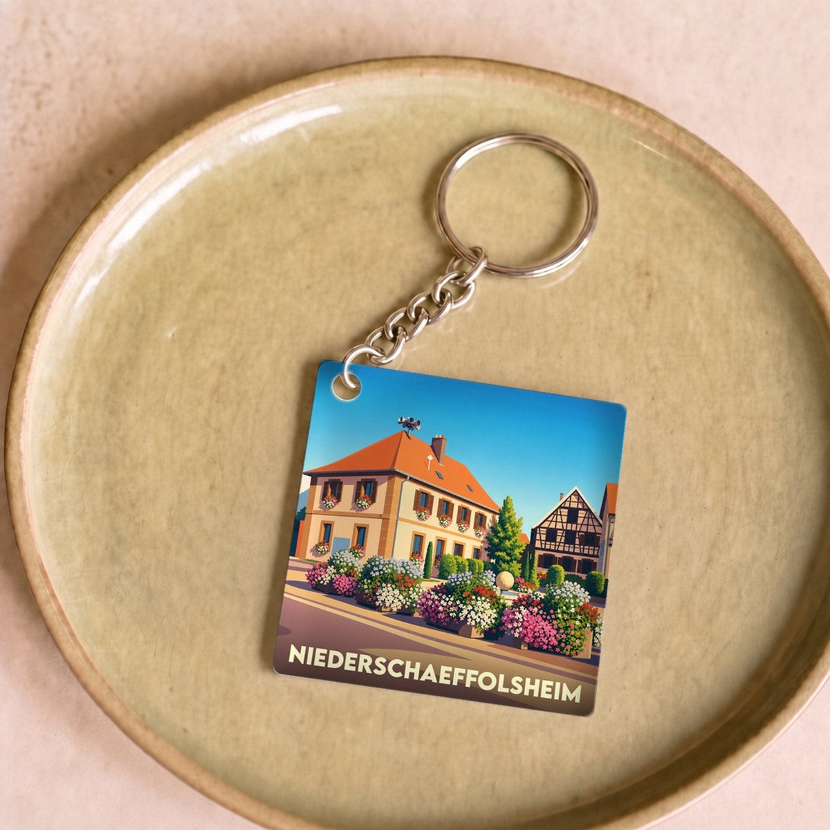 Porte-clés souvenir de la ville de Niederschaeffolsheim avec une illustration stylisée d'une maison fleurie.