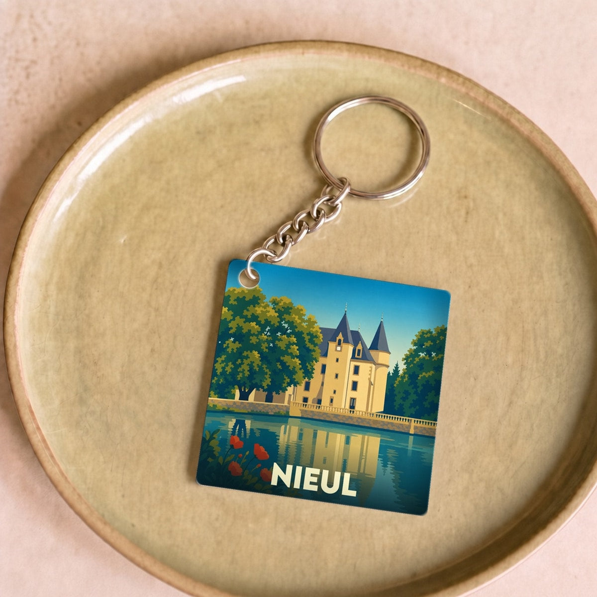 Porte-clés souvenir de la ville de Nieul avec une illustration stylisée de son château se reflétant dans l'eau.