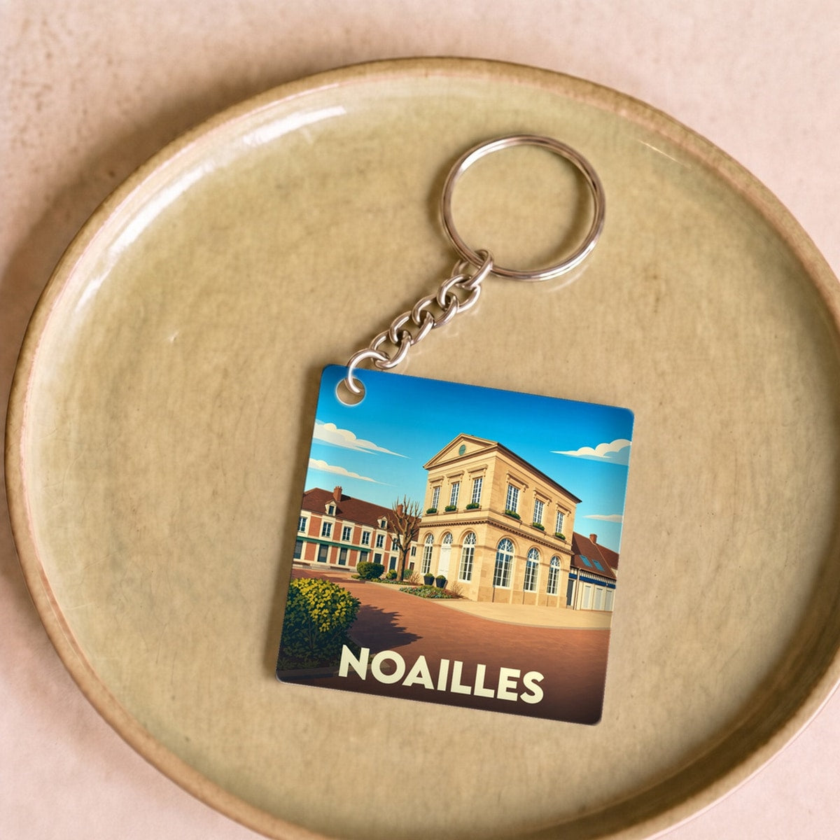 Porte-clés souvenir de la ville de Noailles avec une illustration stylisée.