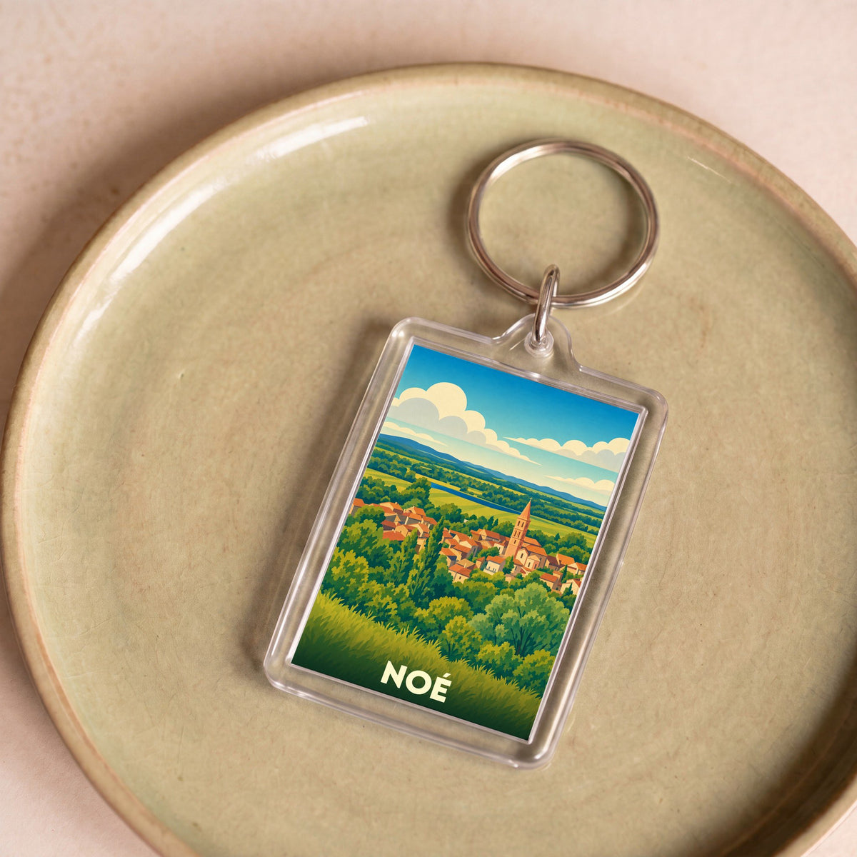 Porte-clés souvenir de la ville de Noé avec une illustration stylisée de son paysage et de son clocher.