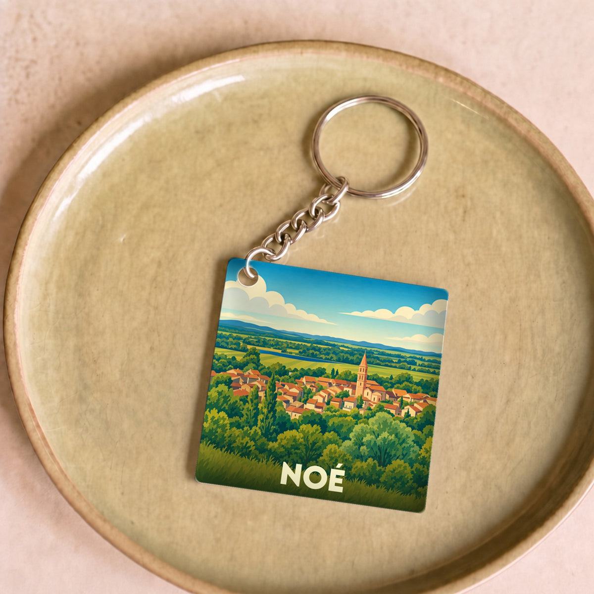 Porte-clés souvenir de la ville de Noé avec une illustration stylisée de son paysage et de son clocher.