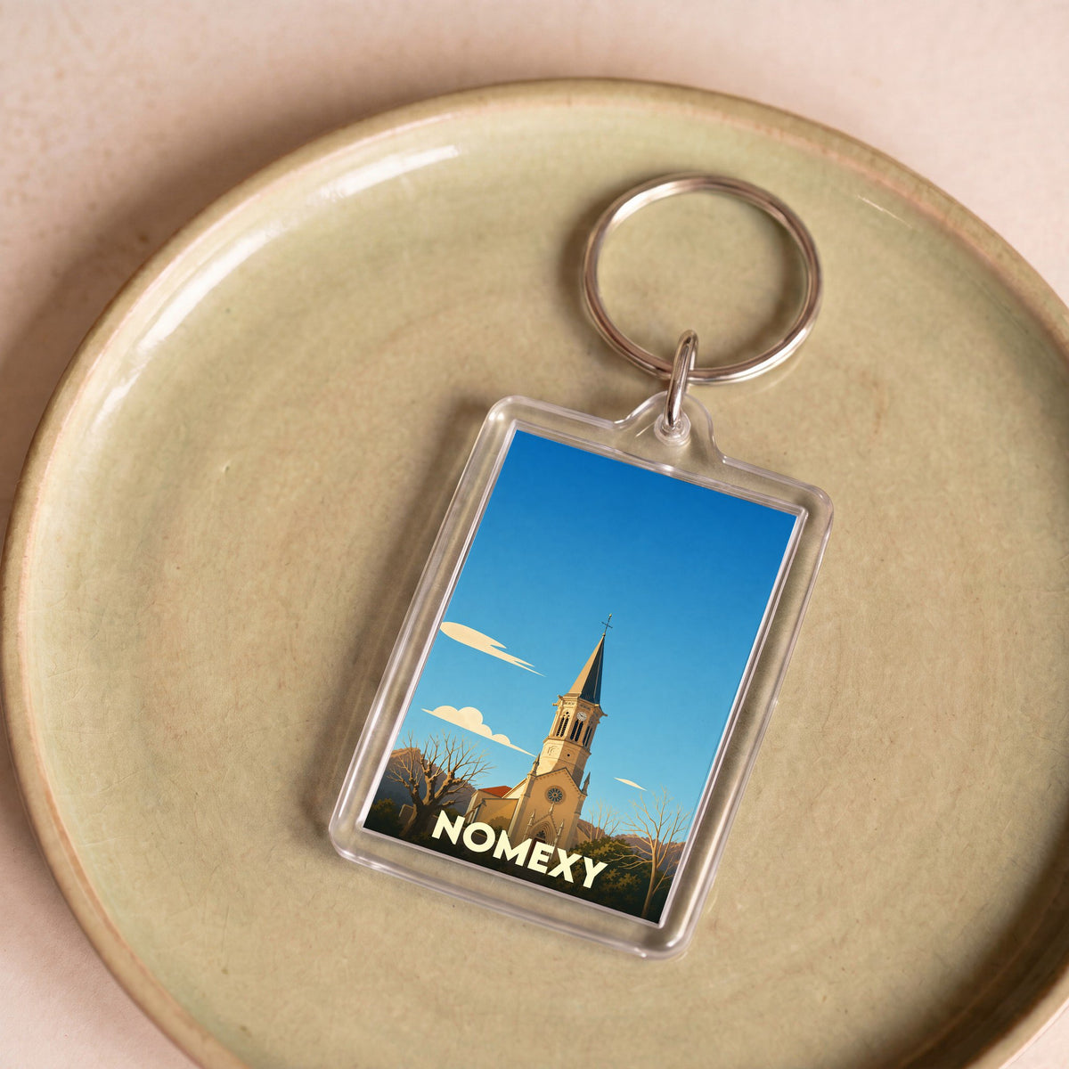 Porte-clés souvenir de la ville de Nomexy avec une illustration stylisée de son église.