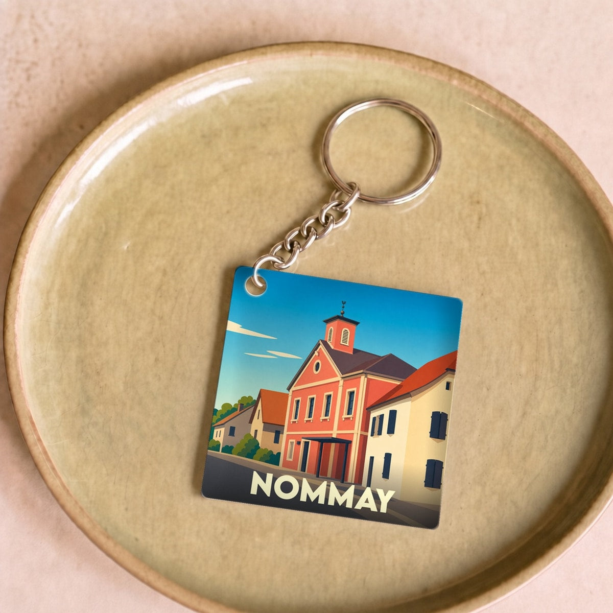 Porte-clés souvenir de la ville de Nommay avec une illustration stylisée.